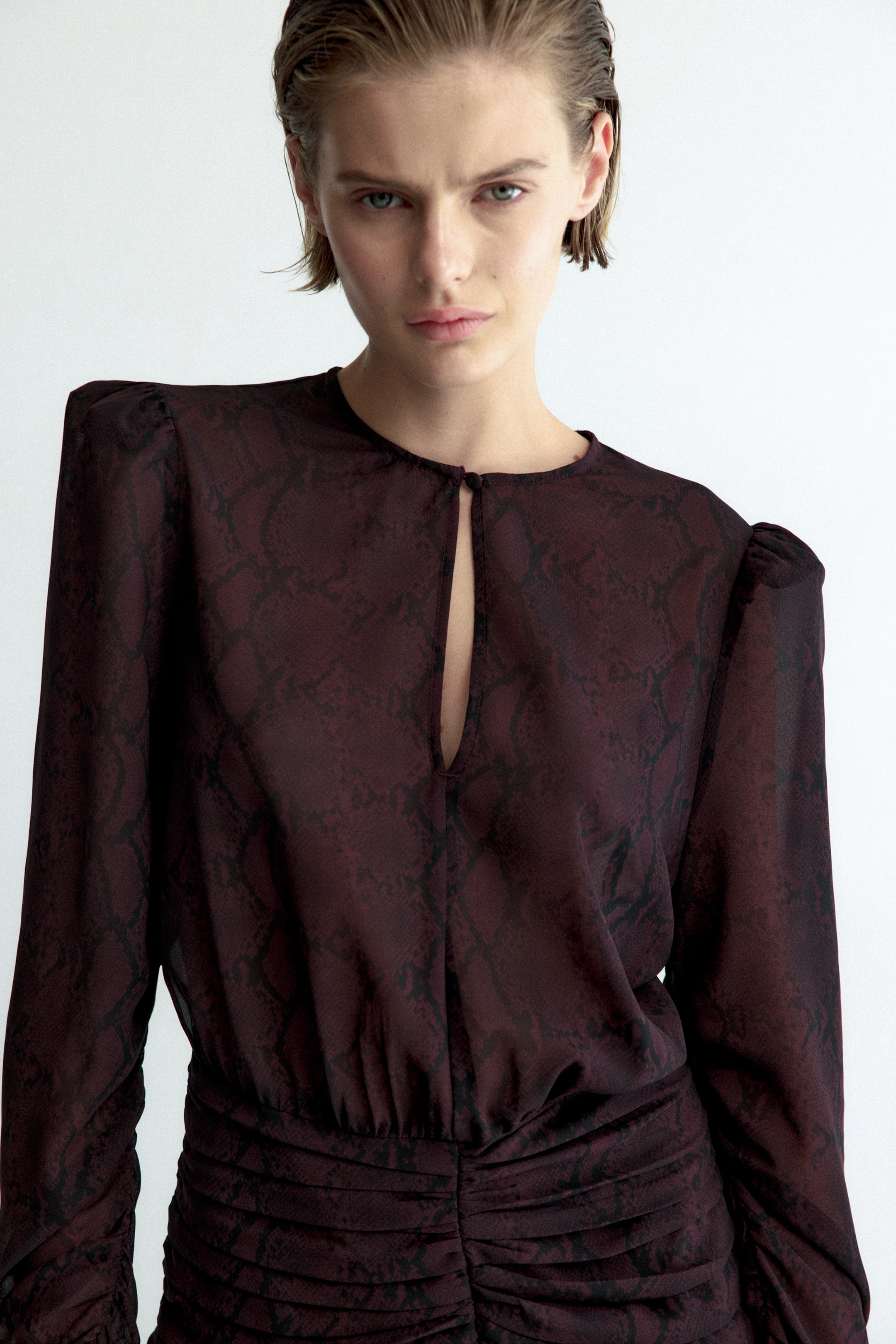 Voir une image plus grande: Une robe en mousseline froncée, avec un imprimé peau de serpent rouge foncé, est portée par le mannequin. La robe présente un col rond avec une ouverture en goutte, des manches longues à épaules bouffantes et des fronces horizontales à la taille.