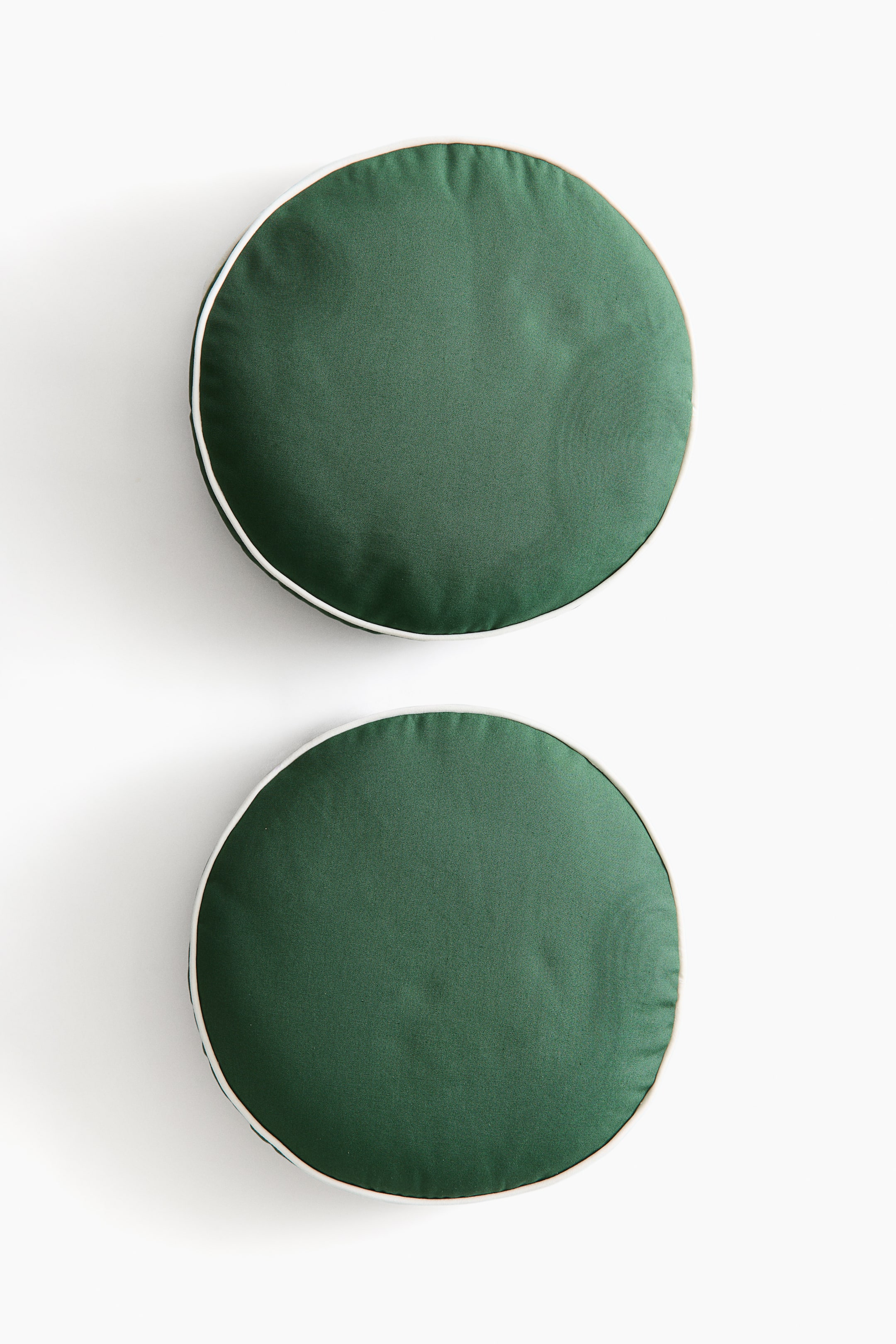 Ampliar la imagen: Dos cojines redondos muestran una tela verde oscuro, cada uno con un ribete blanco alrededor de su borde circular.
