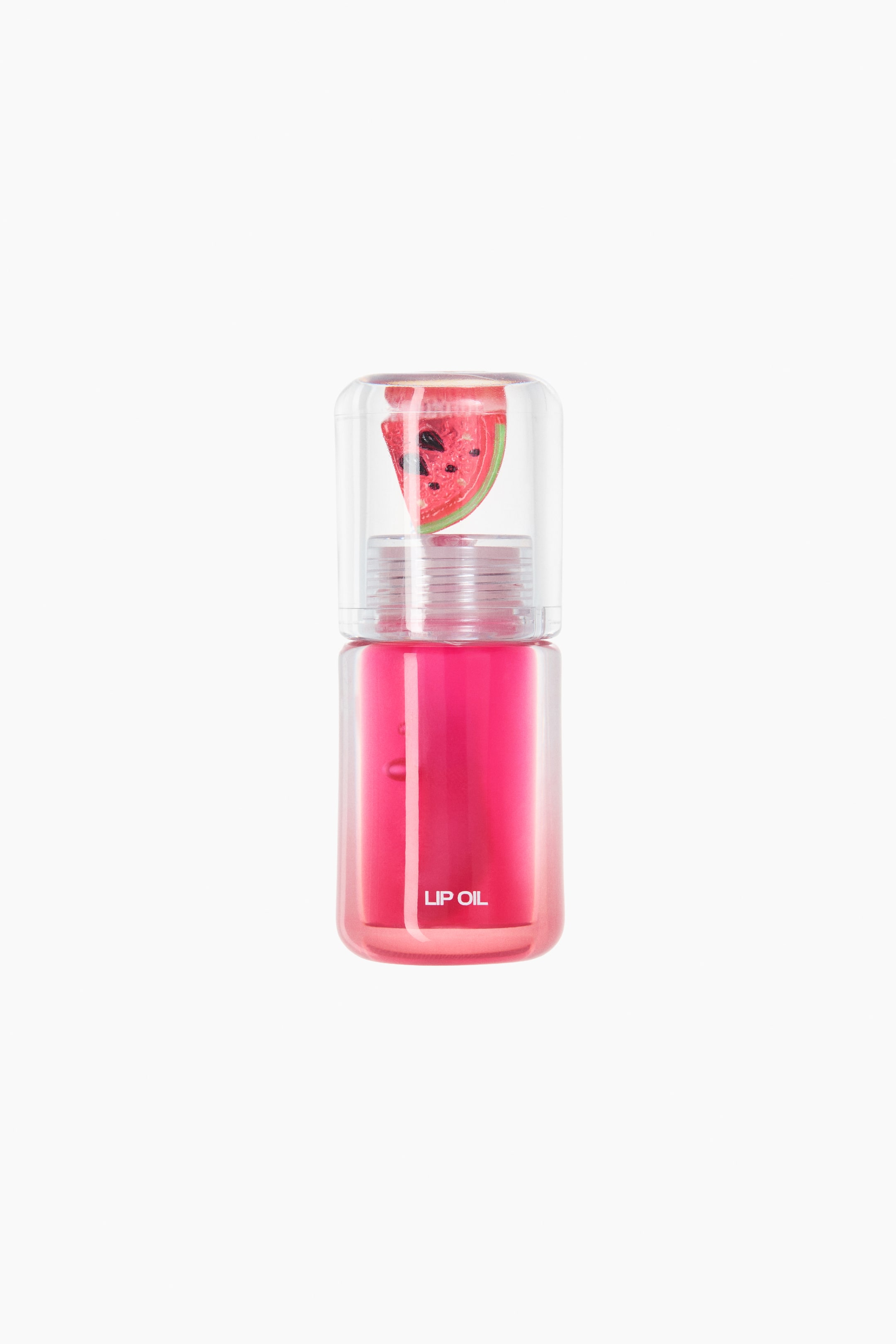 View larger image: A lip oil bottle stands in the foreground, filled with vibrant pink liquid and topped with a clear cap that showcases a watermelon slice design inside.
