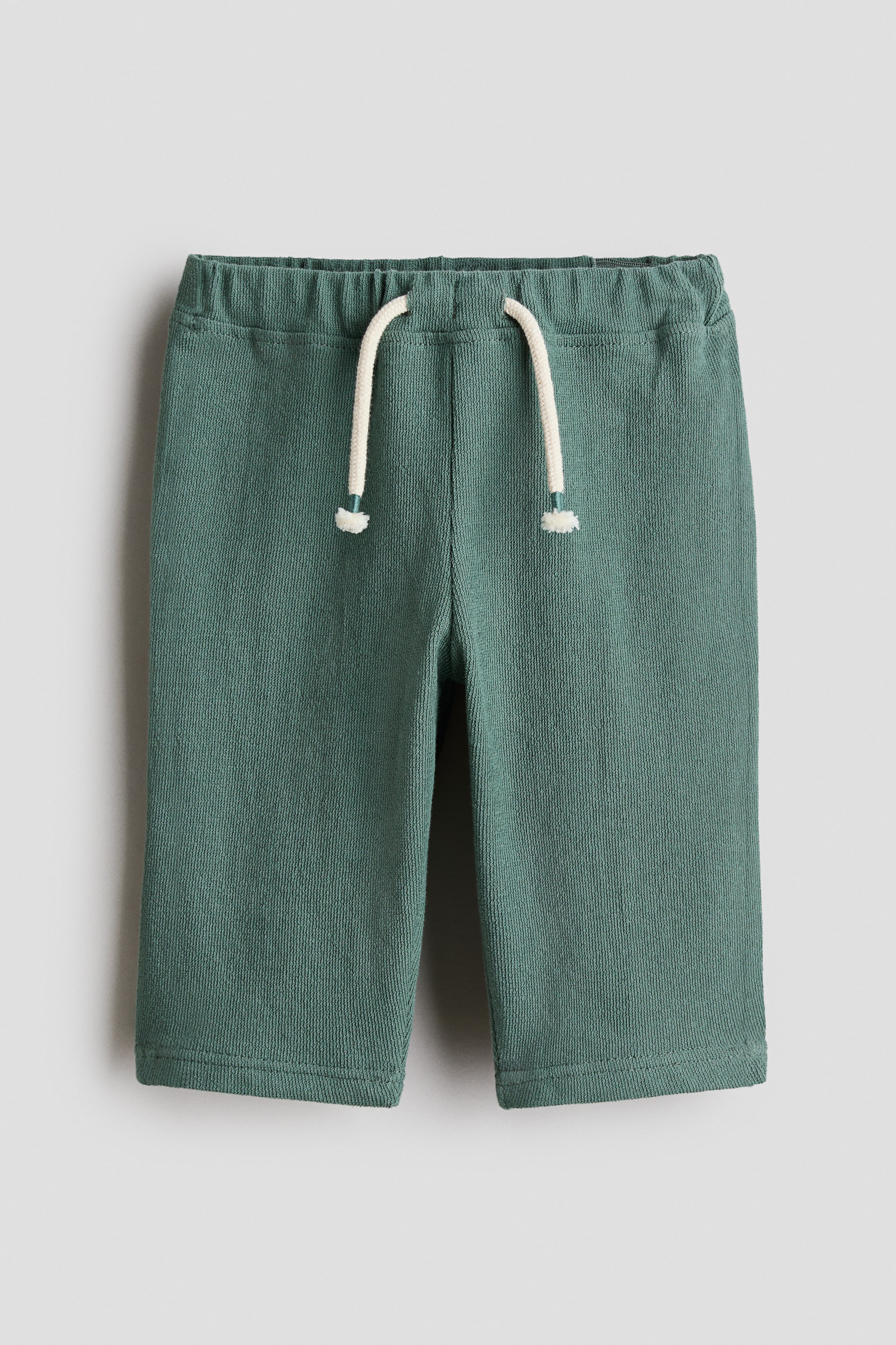 Xem ảnh lớn hơn: Quần lửng màu xanh teal đậm có kết cấu gân mảnh và phần eo chun co giãn. Một sợi dây rút màu trắng ngà với đầu mút màu xanh nổi bật ở phía trước eo.