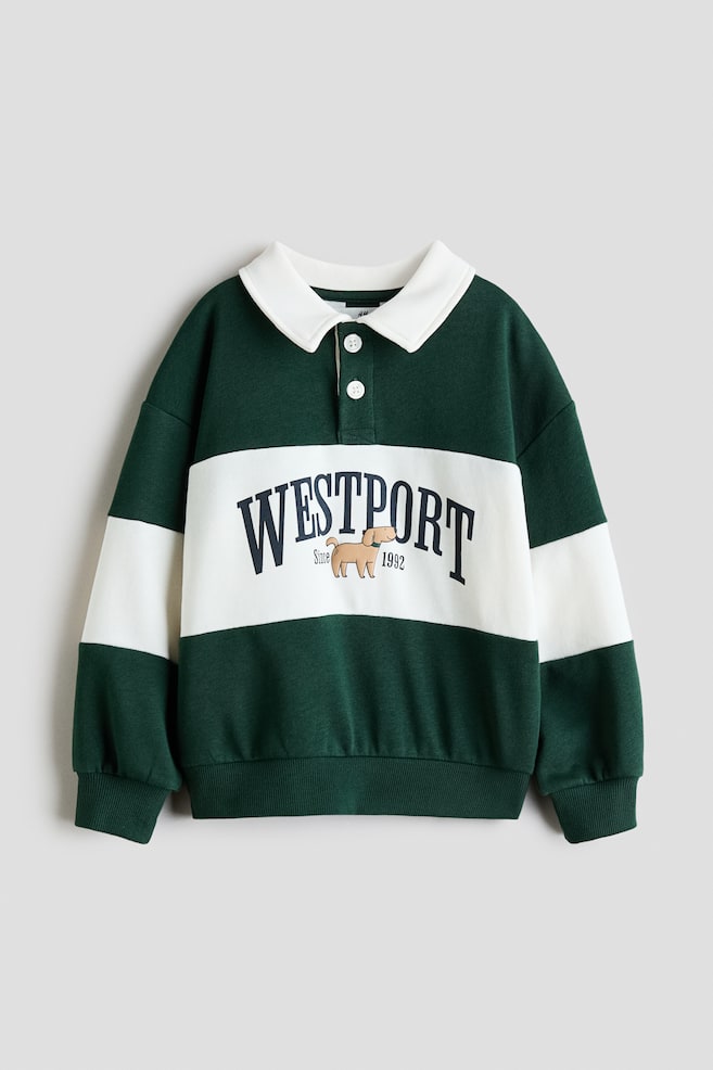 A long-sleeved polo sweatshirt is displaying a dark green and white horizontal stripe pattern, featuring a white collar with a two-button placket. The central white stripe is showcasing "WESTPORT Since 1992" lettering with a small brown dog graphic, and the sweatshirt is finished with dark green ribbed cuffs and hem. - 1