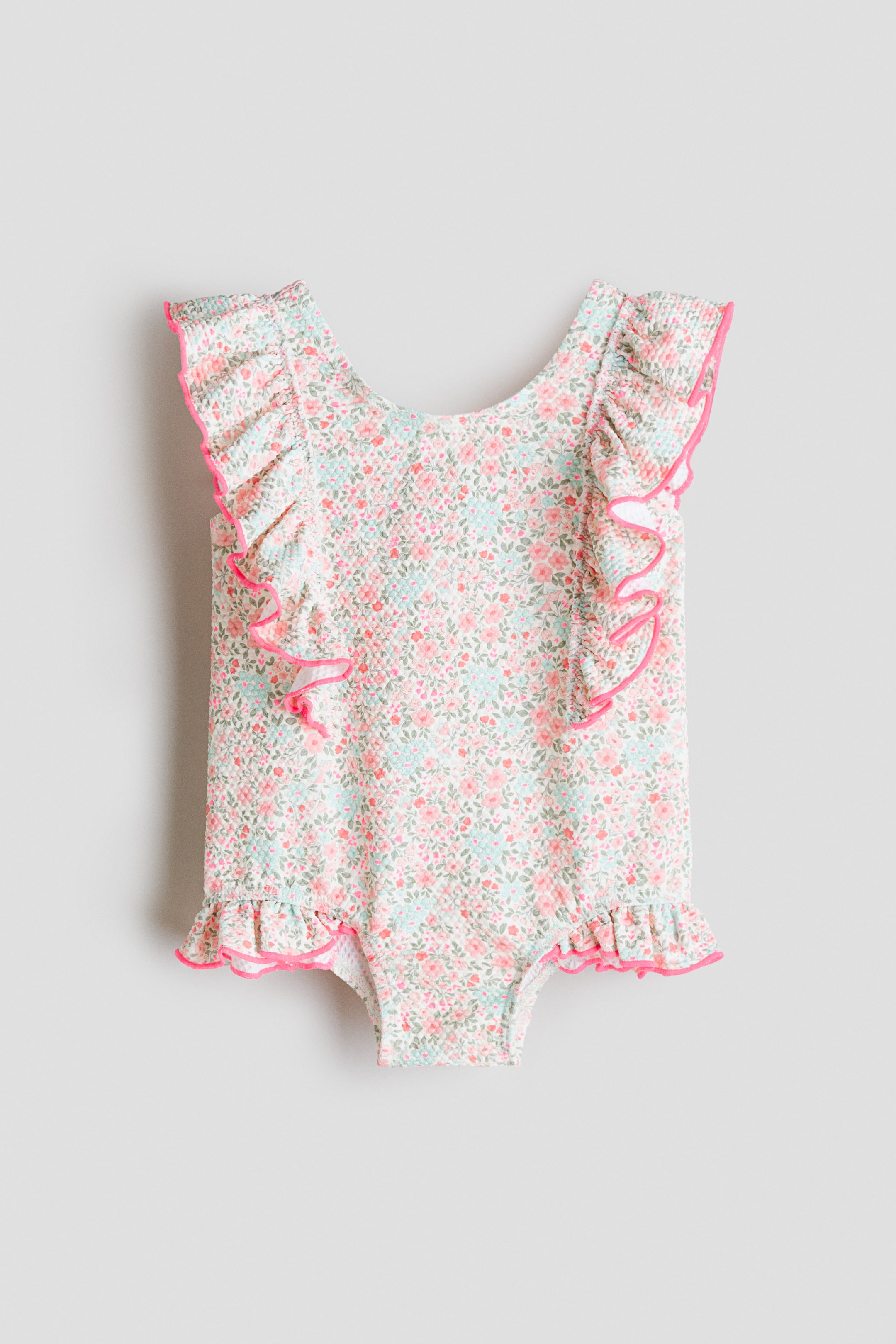View larger image: The swimsuit is displayed from the front, showcasing a textured fabric with a delicate floral pattern in shades of pink, light blue, and green. Frill trims with vibrant pink edges accentuate the shoulders and leg openings.