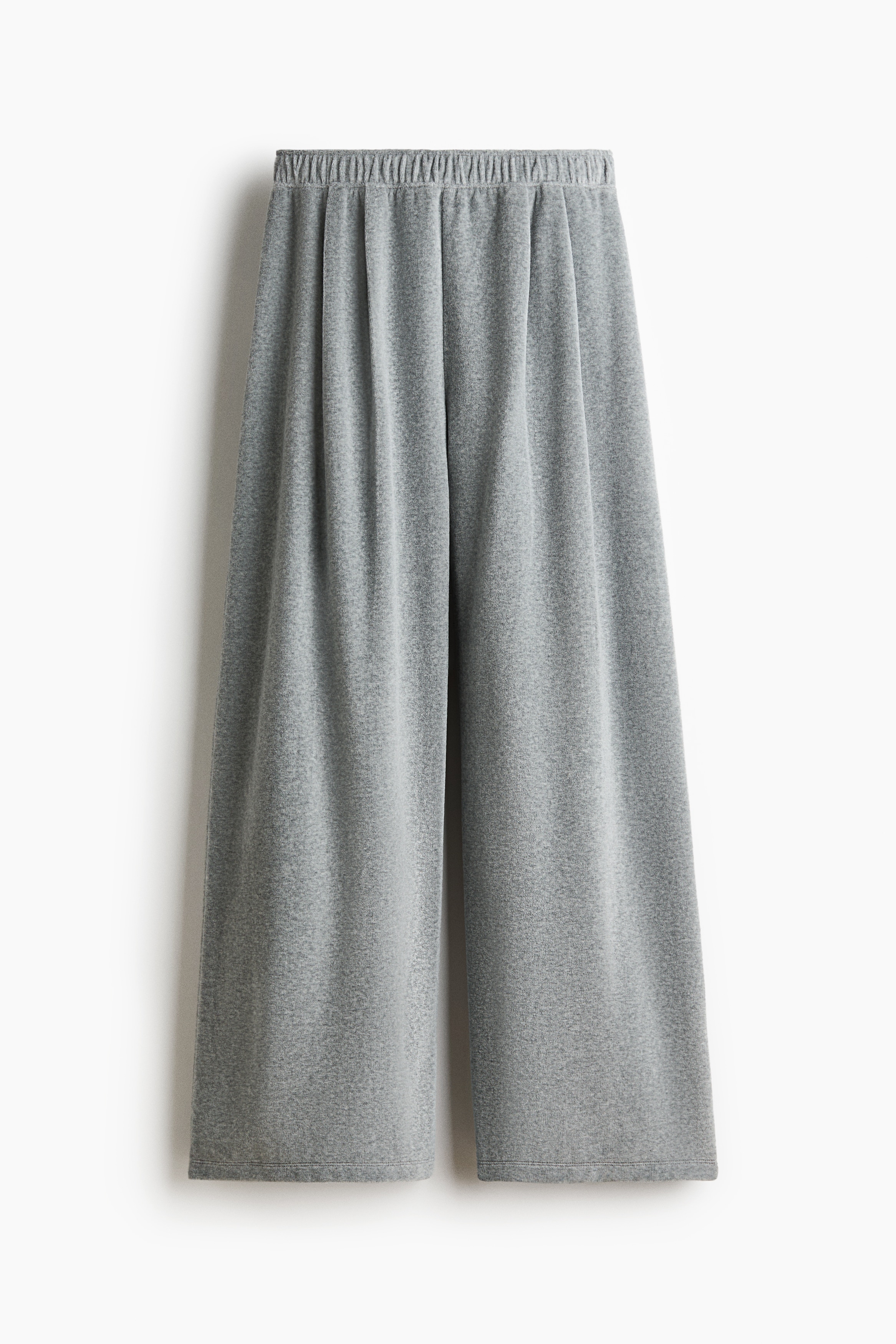 The model is wearing grey cotton-blend velour joggers featuring an elasticized waistband and straight legs with front pleats. The joggers are paired with a matching grey velour zip-up jacket and a white cropped tank top.