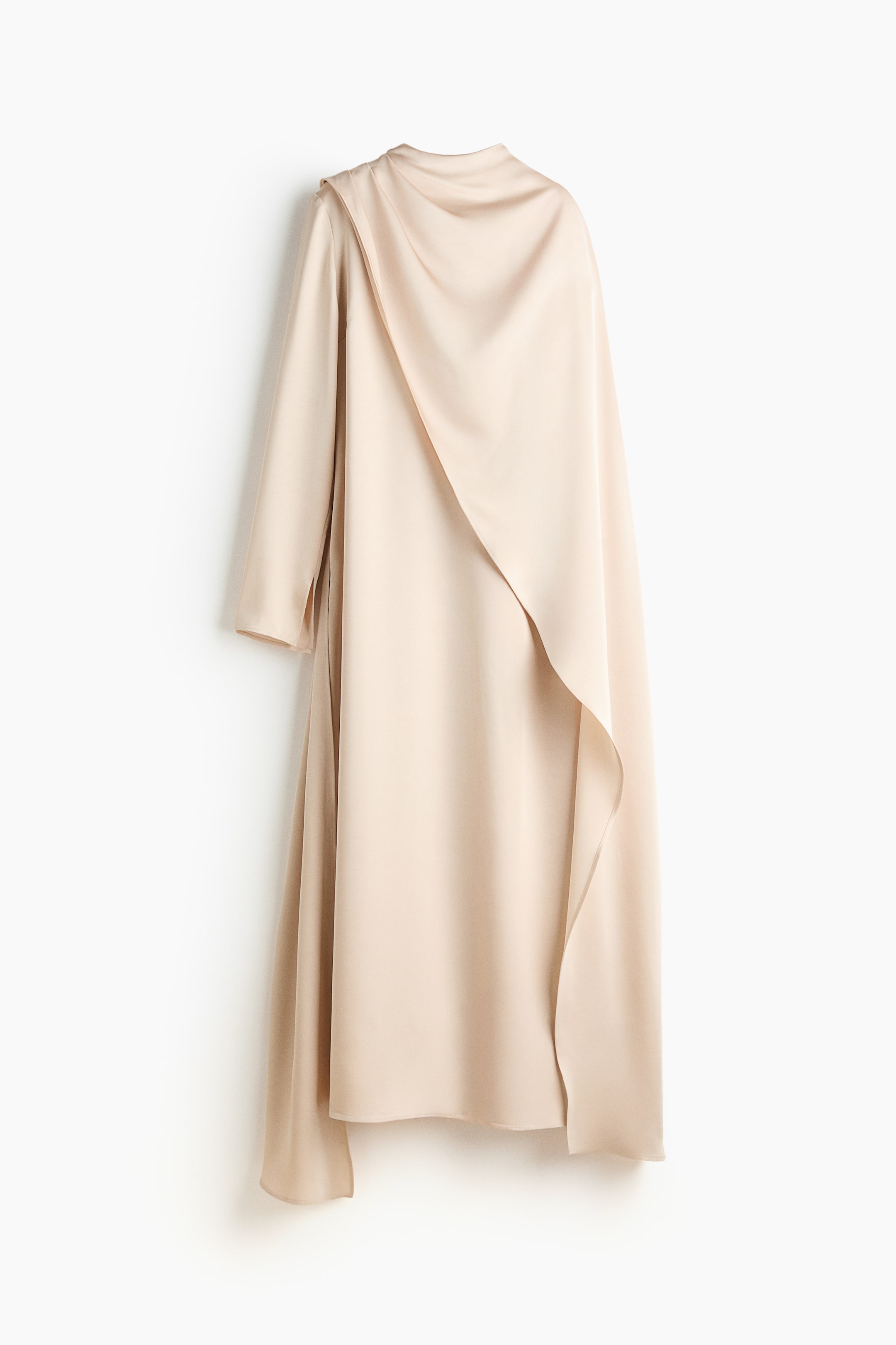 View larger image: A pale beige, satiny long garment is draped, facing FRONT, showing a high neckline, long sleeves, and a large, asymmetrical panel flowing from the left shoulder across the front, creating soft folds and an uneven hemline.