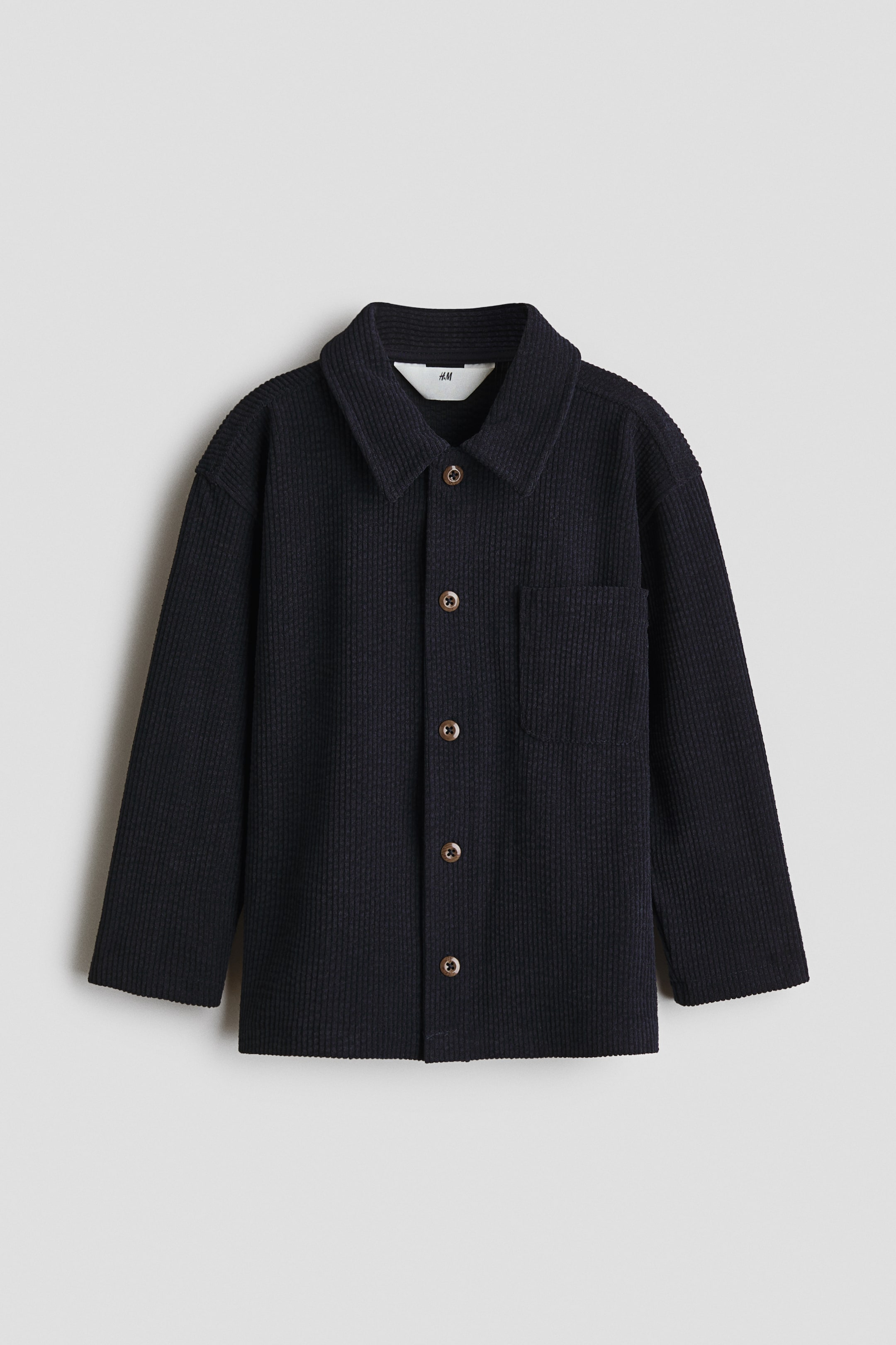 View larger image: A black waffle-knit shirt jacket is shown from the front, featuring a pointed collar, a row of brown buttons down the front, and a single chest patch pocket.