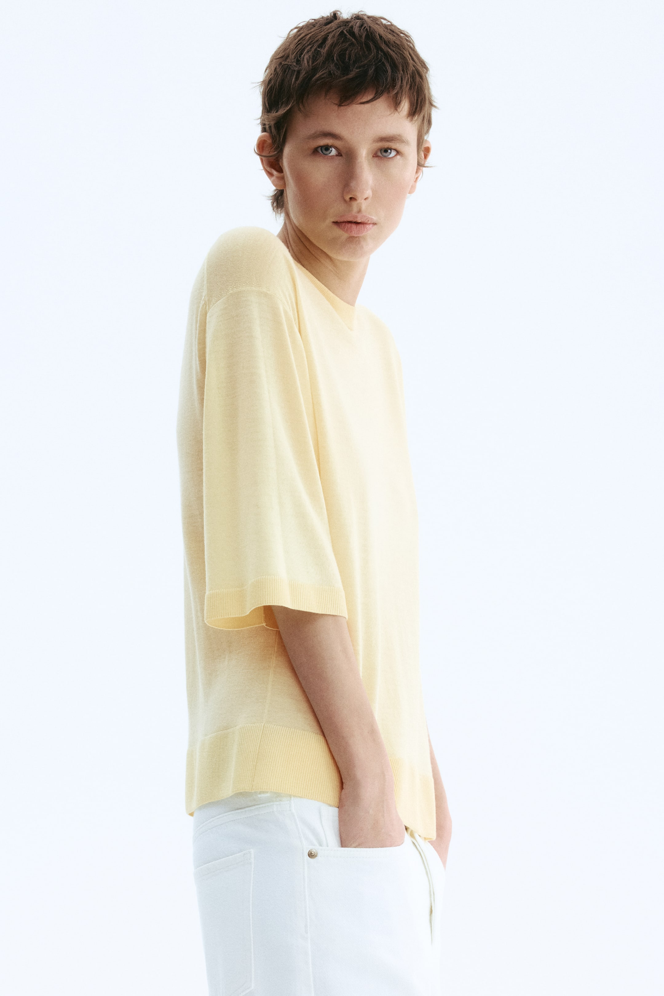 View larger image: A light yellow short-sleeved knit top is presenting a relaxed fit with a crew neck, wide elbow-length sleeves featuring ribbed cuffs, and a ribbed hem. The top is angled slightly to the left, highlighting its structure.