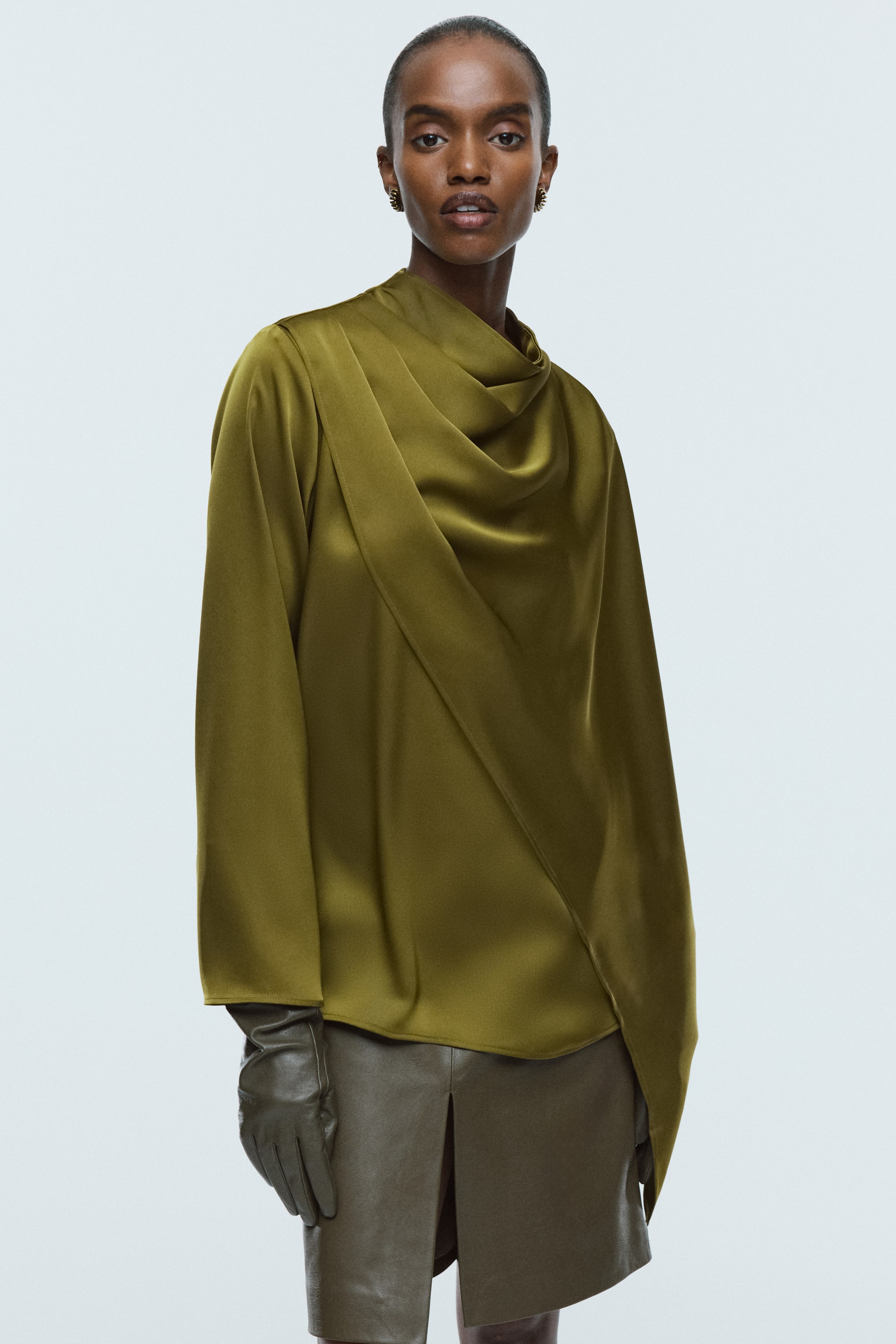 View larger image: A lustrous olive green satin blouse, featuring a stand collar, long sleeves, and a prominent shawl detail draped across the front, is being worn by the model.
