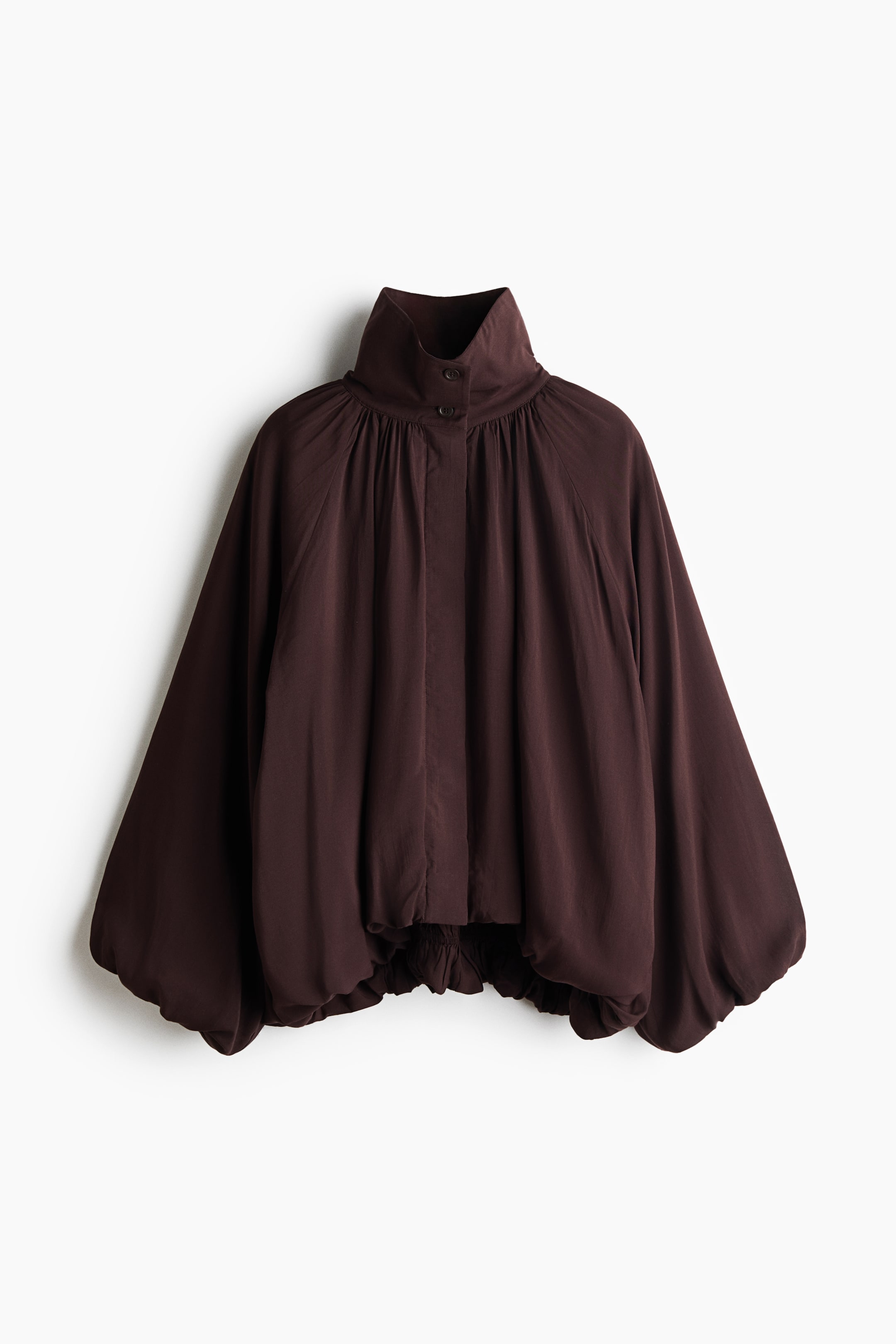 View larger image: This loose-fit, dark brown jacket is shown from the front, featuring a high, buttoned funnel collar and a concealed front button placket. The design features voluminous raglan sleeves with elasticated cuffs and an elasticated bubble hem that creates a puffy, gathered silhouette.