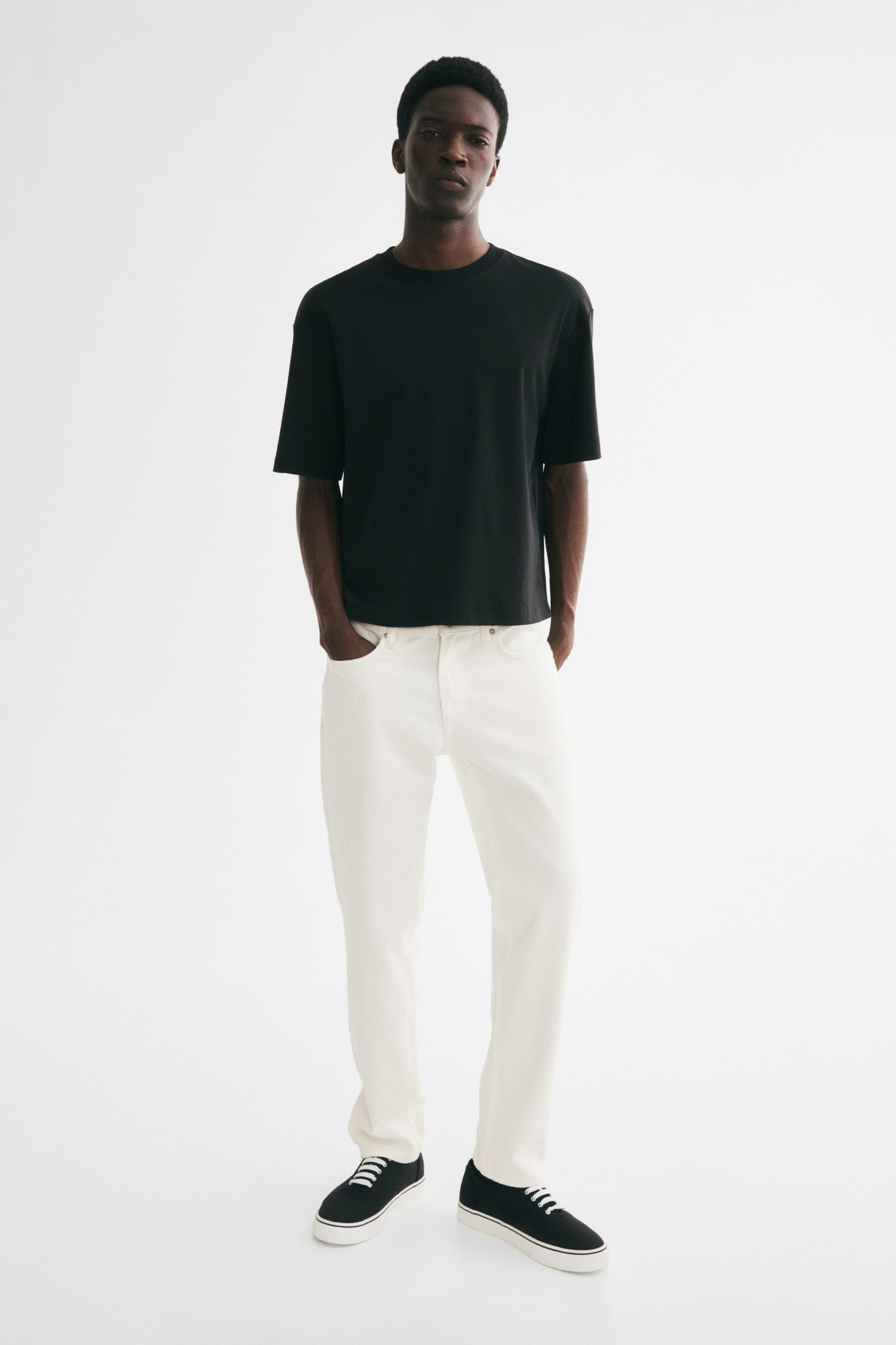 View larger image: Off-white 5-pocket cotton denim jeans, featuring a regular waist, straight legs, and a slim fit from the waist through the thigh to the hem, are being worn by the model. The model is placing hands into the front pockets of the jeans.