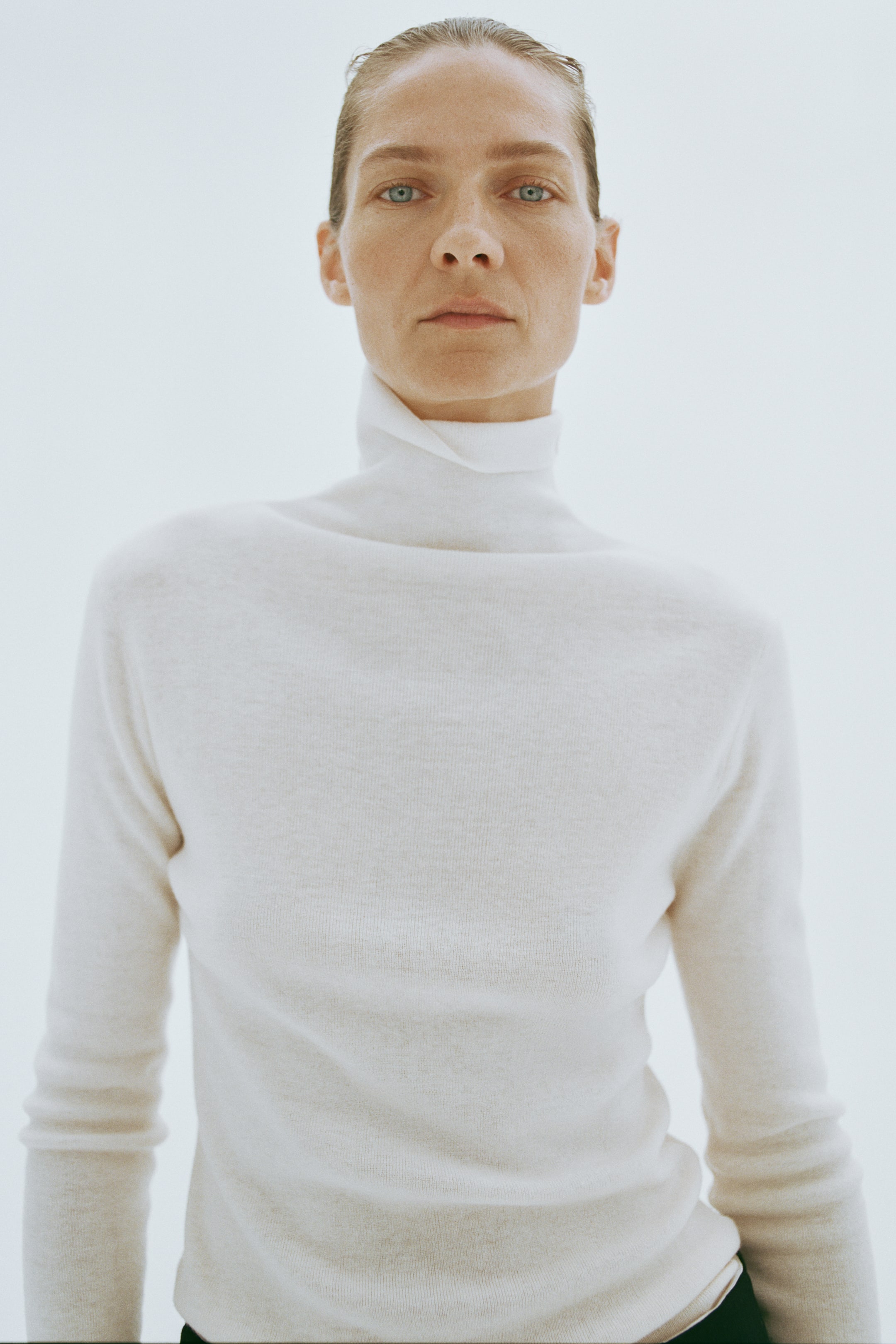 Agrandir l'image: Le mannequin porte un pull à col roulé en maille fine, de couleur crème, doté d’une silhouette ajustée et d’un col haut et souple. Le pull présente des épaules légèrement tombantes et des manches longues, légèrement froncées aux poignets.