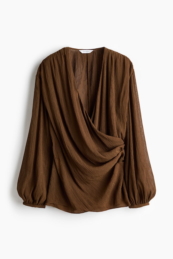 A brown blouse in a crinkled weave is facing front, featuring a deep V-neckline and a sewn-in wrapover front that creates a draped, gathered effect. The design is showcasing long balloon sleeves that finish with narrow cuffs. - 1