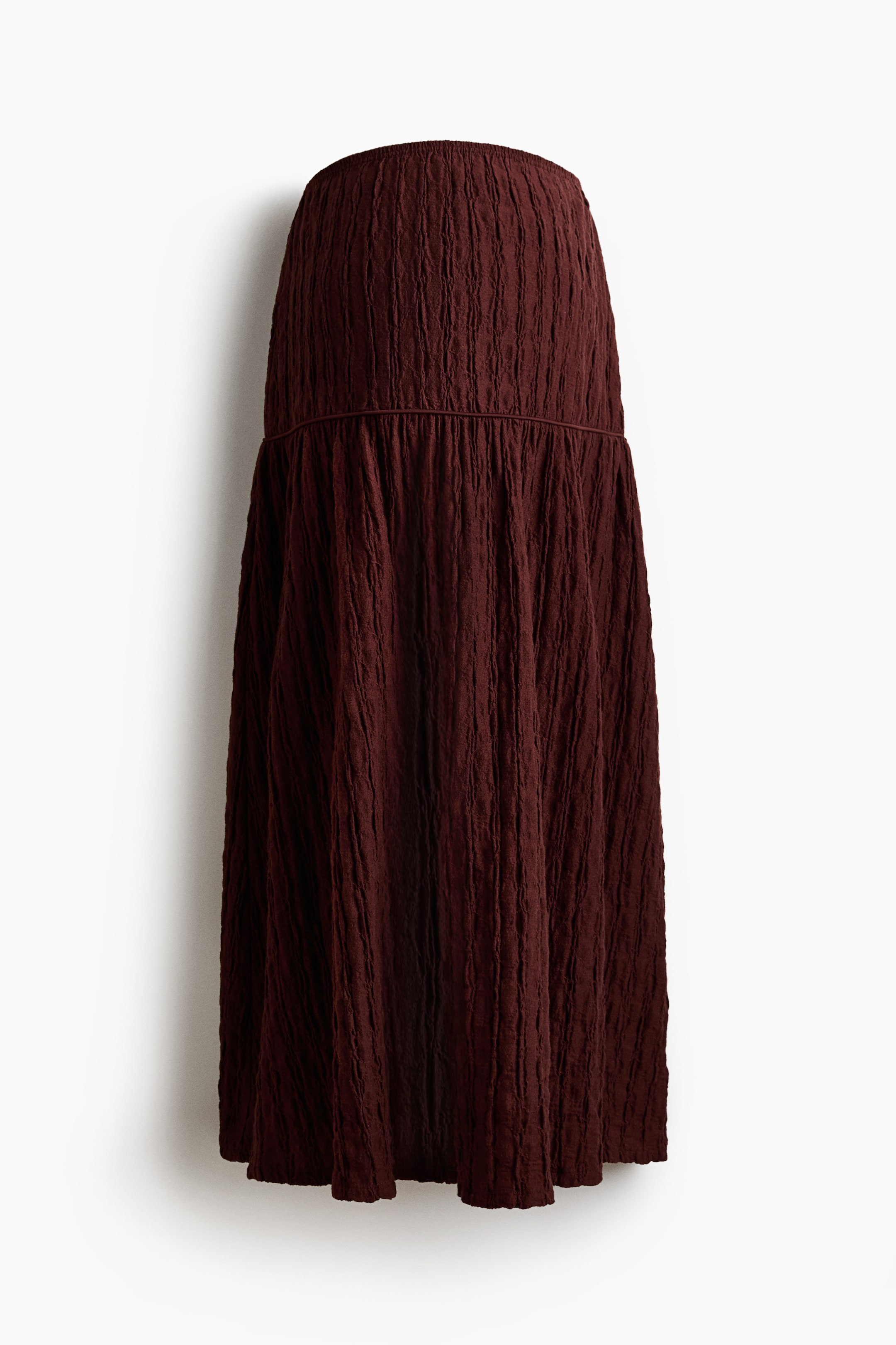 Ampliar la imagen: Una falda roja oscura de línea A hasta la pantorrilla se muestra desde el frente, confeccionada en un material de jersey texturizado, con una cintura elástica cubierta y una costura fruncida con ribete debajo de las caderas.