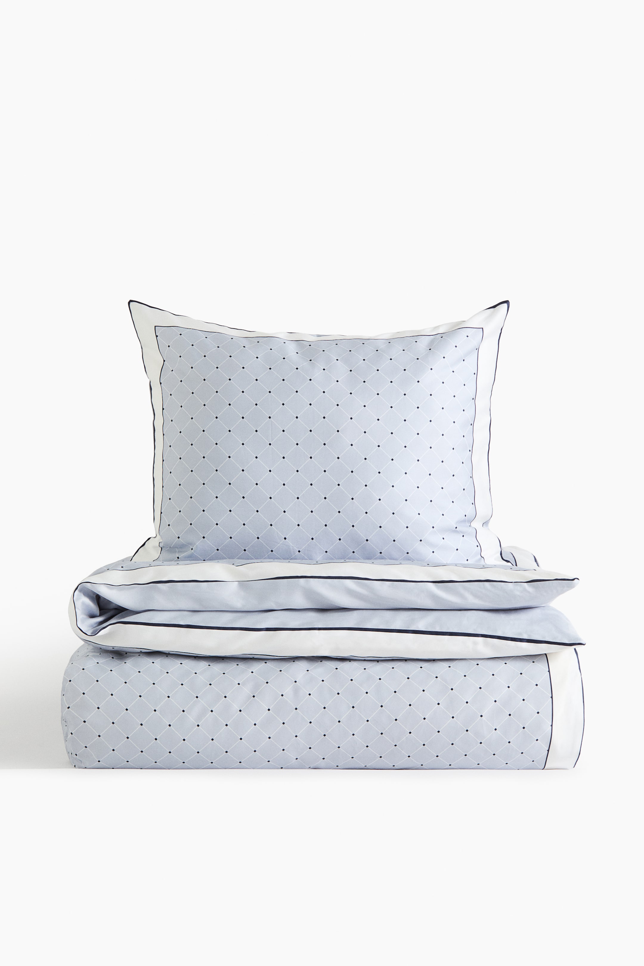 View larger image: A duvet cover set features a light blue fabric with an all-over diamond grid pattern and dark dots. A folded duvet cover lies at the bottom, and a matching pillowcase rests on top, both featuring a white accent border with dark piping along the edges.