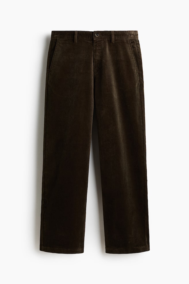 Dark brown corduroy trousers are lying flat, presenting a front view. They are constructed from a textured corduroy fabric with vertical ridges, featuring a waistband with belt loops, a button and zipper closure, and side slash pockets. - 1