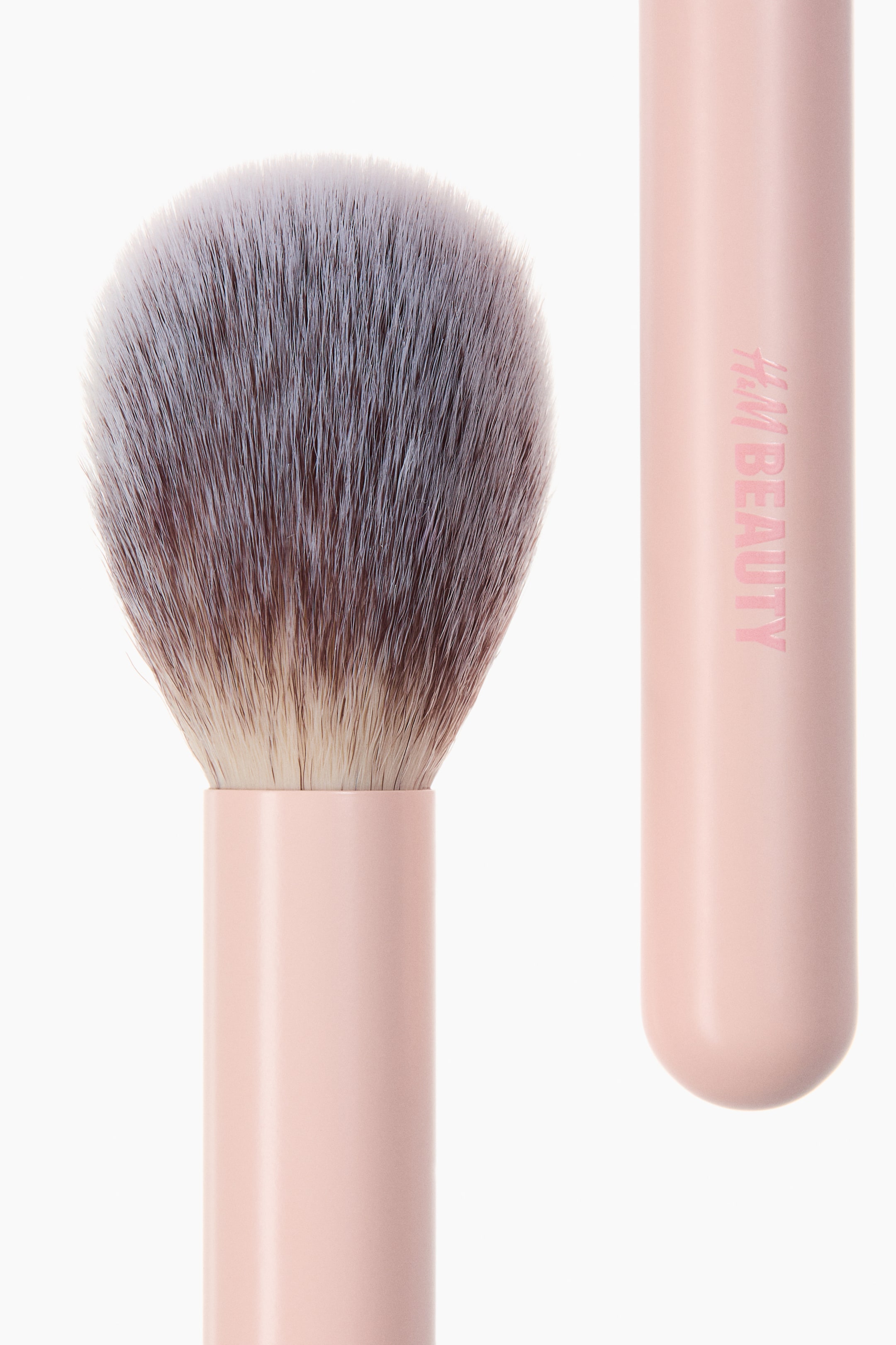 View larger image: A makeup brush is displaying its rounded, fluffy head, which is featuring densely packed bristles transitioning from light beige at the base to white at the tips. The bristles are secured in a light pink cylindrical ferrule, which forms the top of the handle.