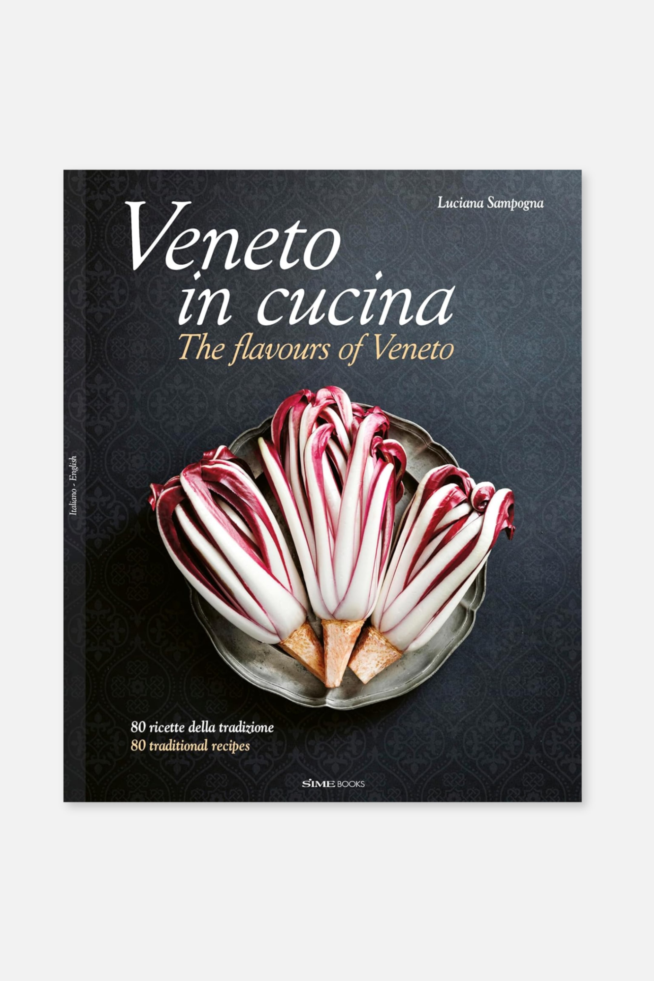 Grotere afbeelding bekijken: Een kookboek getiteld "Veneto in cucina: De smaken van Veneto" staat naar voren gericht, iets naar rechts gekanteld, en toont zijn donkere omslag. De omslag toont verschillende hoofden van rode en witte radicchio gerangschikt op een zilveren gegolfd bord, met tekst die ook "80 traditionele recepten" aangeeft.