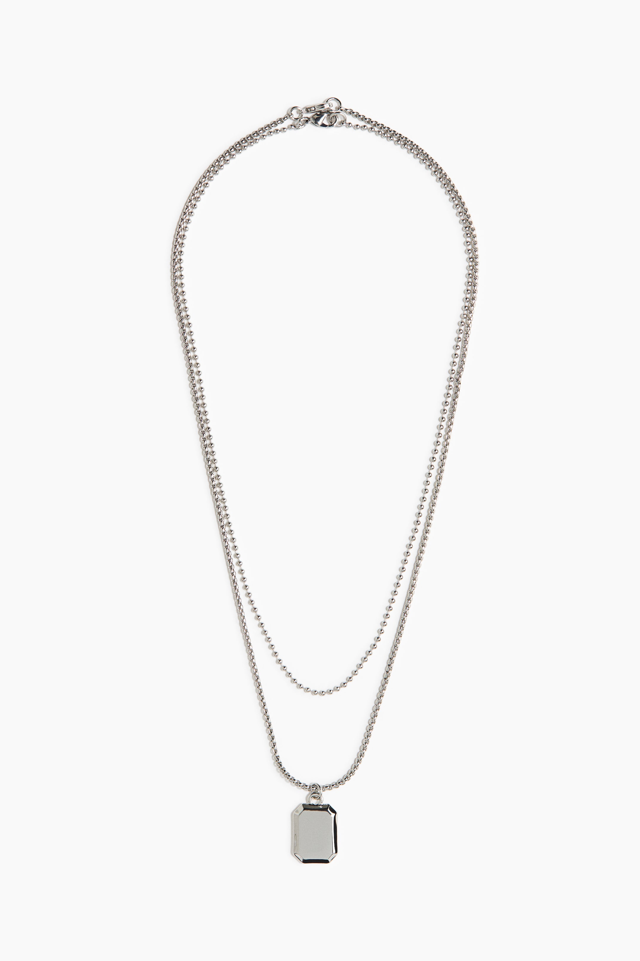 View larger image: A silver-toned layered necklace featuring two ball chains of varying lengths, joined by a lobster clasp at the top. The longer chain suspends a rectangular, faceted silver-toned pendant.