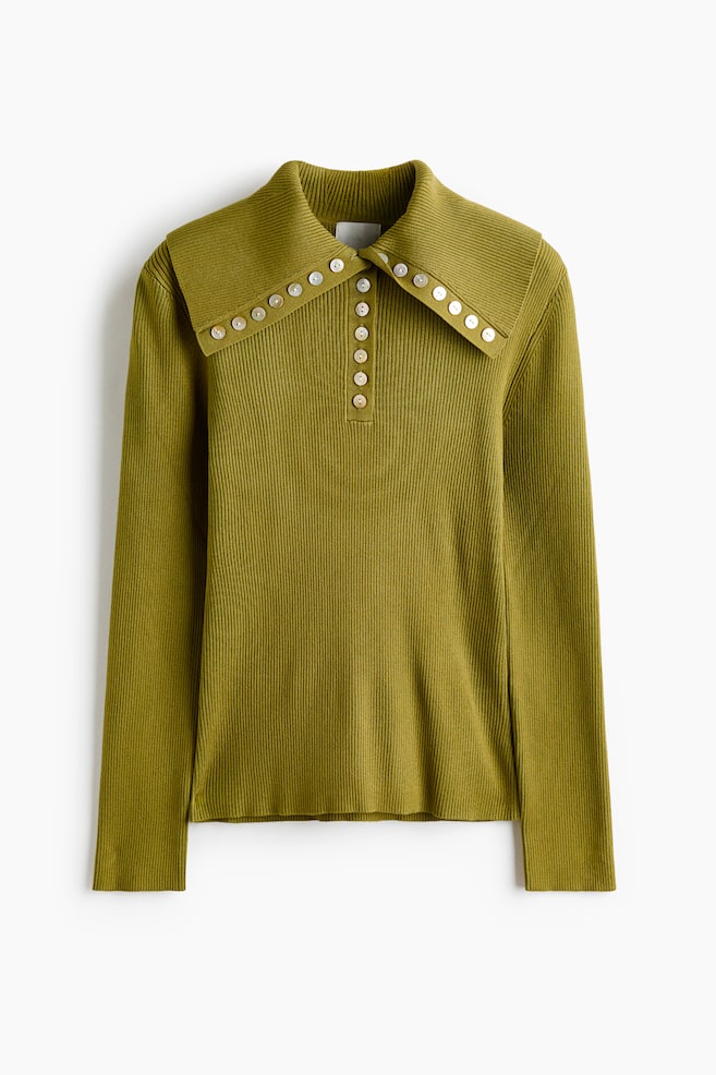 Un top tricotat cu model striat, de culoare verde mÄsliniu, este prezentat din faÈÄ, avÃ¢nd un guler lat, ascuÈit, conturat de-a lungul marginilor cu nasturi decorativi albi. Topul prezintÄ o fente centralÄ parÈialÄ cu nasturi albi asortaÈi Èi are mÃ¢neci lungi, cu o texturÄ finÄ, striatÄ pe toatÄ suprafaÈa. - 1