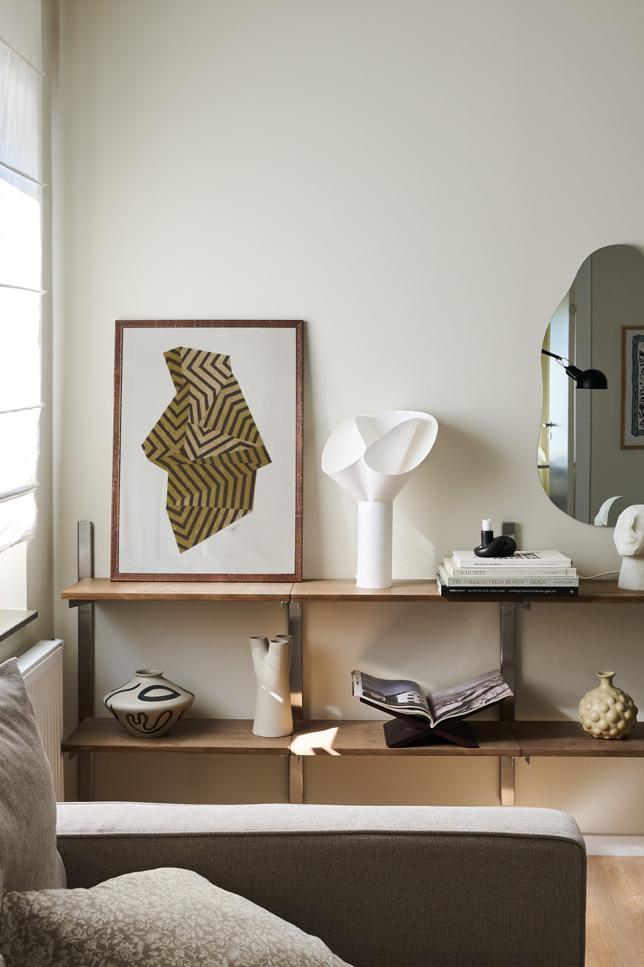 Grotere afbeelding bekijken: De witte sculpturale tafellamp heeft een stevige cilindervormige basis die een organische, bloemachtige kap ondersteunt, gemaakt van gebogen, overlappende witte platen. De lamp staat rechtop op een houten plank en toont zijn gladde matte afwerking en architectonische vorm.