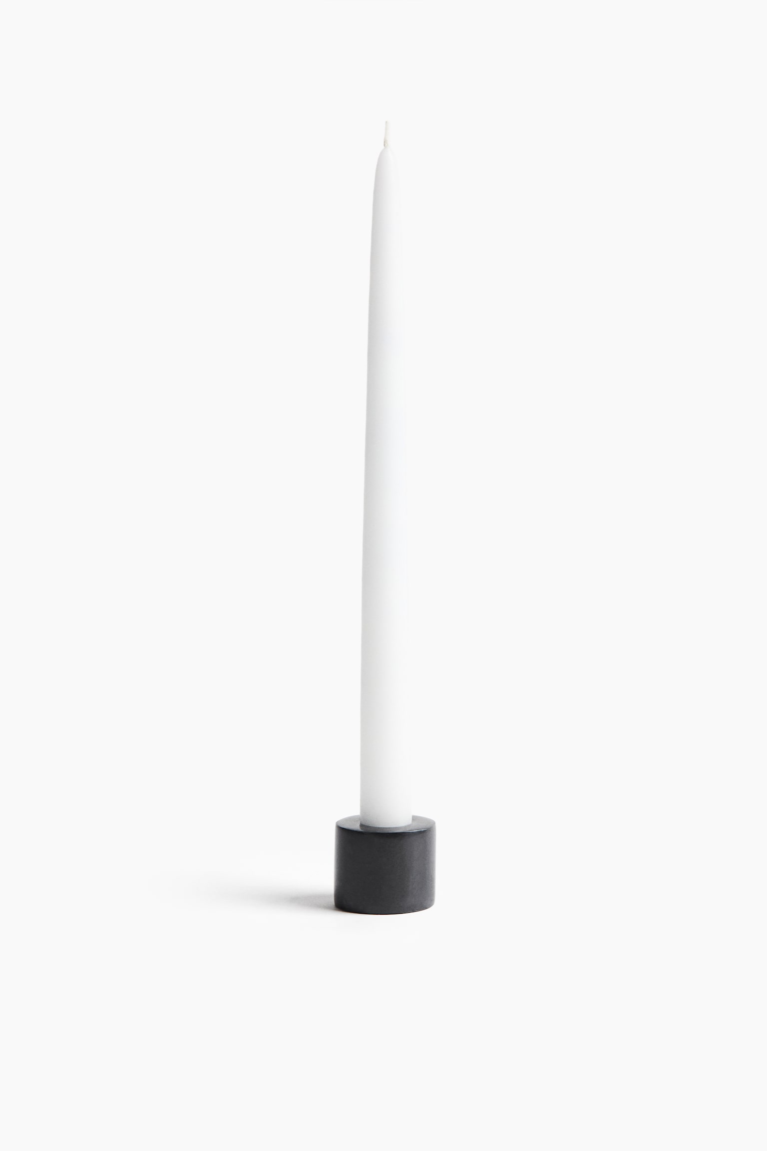 Une grande bougie conique blanche est debout Ã  la verticale, maintenue dans un petit support cylindrique gris foncÃ©. La bougie sâamincit progressivement vers son sommet, oÃ¹ lâon voit une courte mÃ¨che blanche.