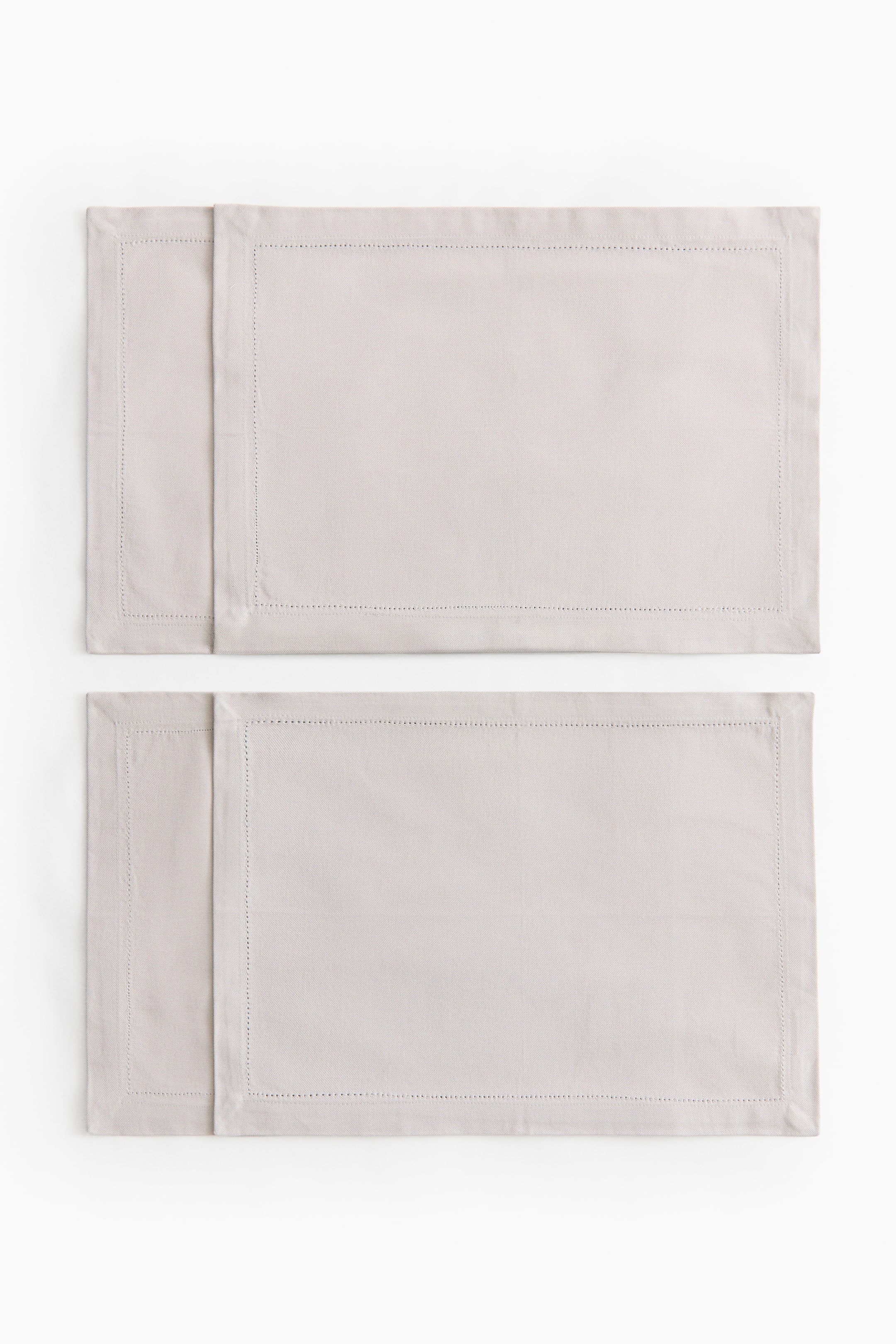 Agrandir l'image: Deux sets de table rectangulaires en toile de coton sont posés à plat, l’un partiellement superposé à l’autre. Chacun présente une couleur claire et neutre ainsi qu’un détail à jours le long de son ourlet de 2,5 cm.