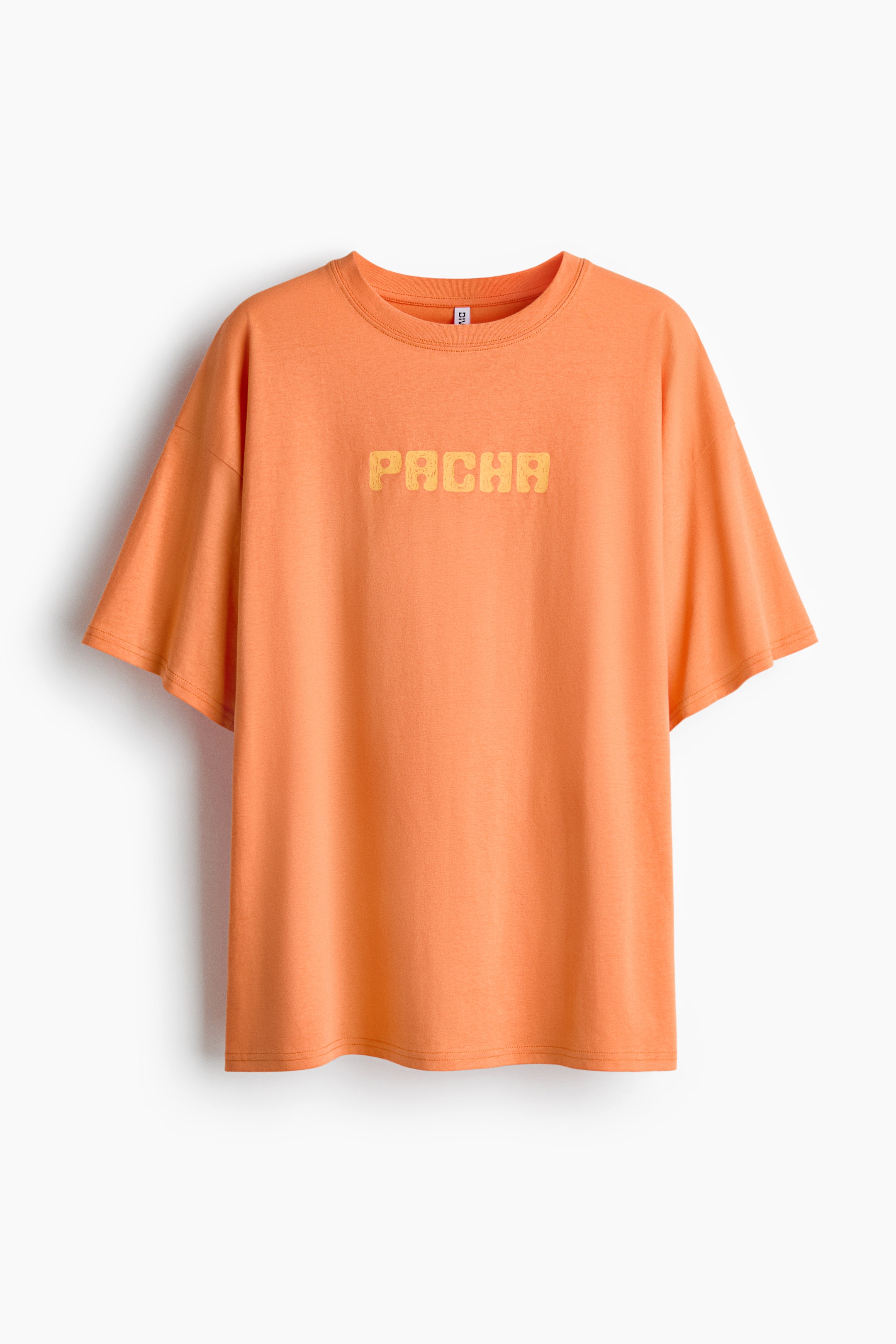 Größeres Bild ansehen: Ein oversizedes, orangefarbenes Baumwoll-Jersey-T-Shirt zeigt seine FRONT: ein runder, mit Rippenbesatz eingefasster Halsausschnitt, überschnittene Schultern und das Wort „PACHA“, das in einer gelben, strukturierten Schrift quer über der Brust aufgedruckt ist.