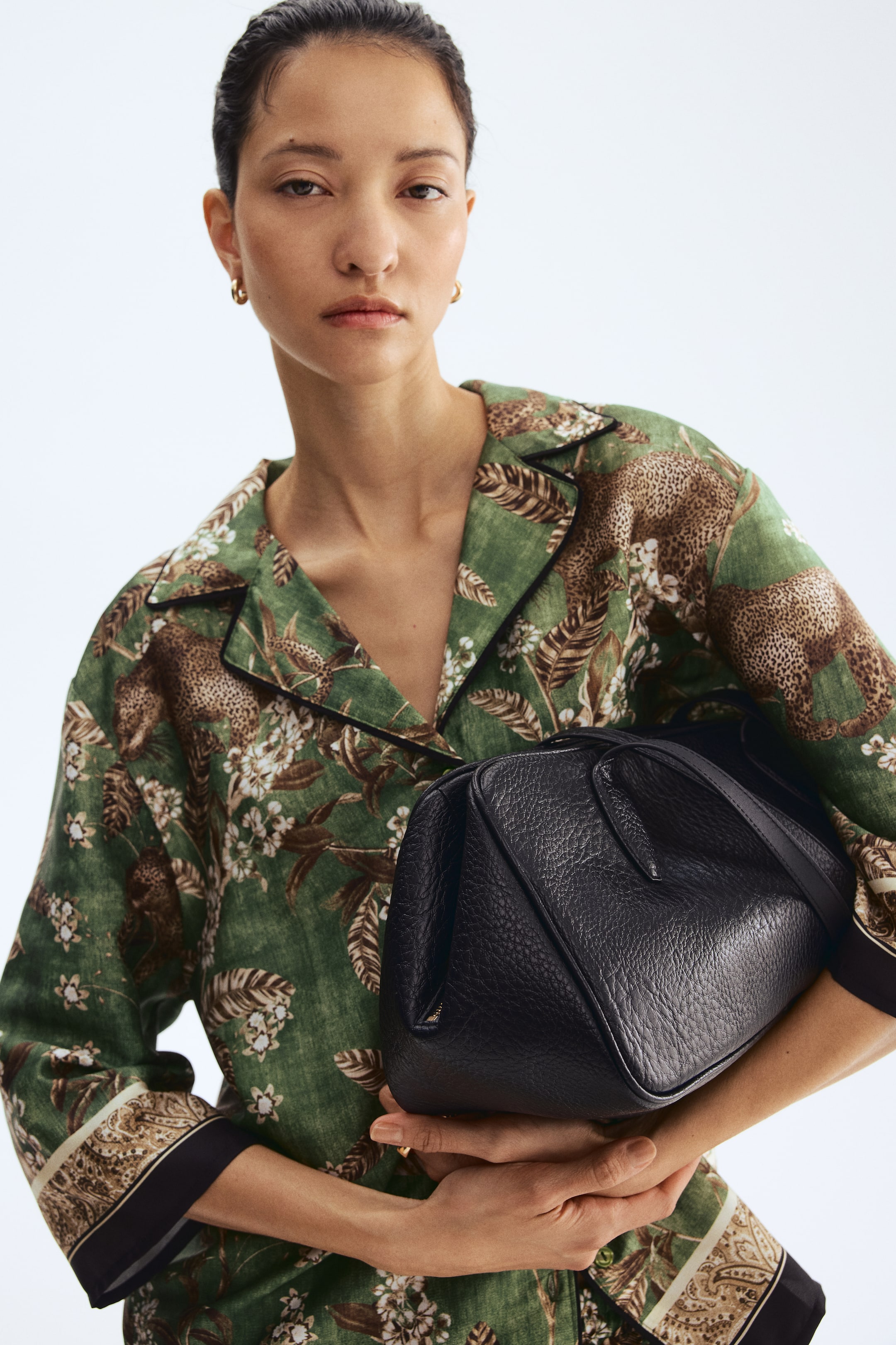 View larger image: A black pebbled leather handbag with a soft, structured shape and a short top handle is being held in both hands by the model.