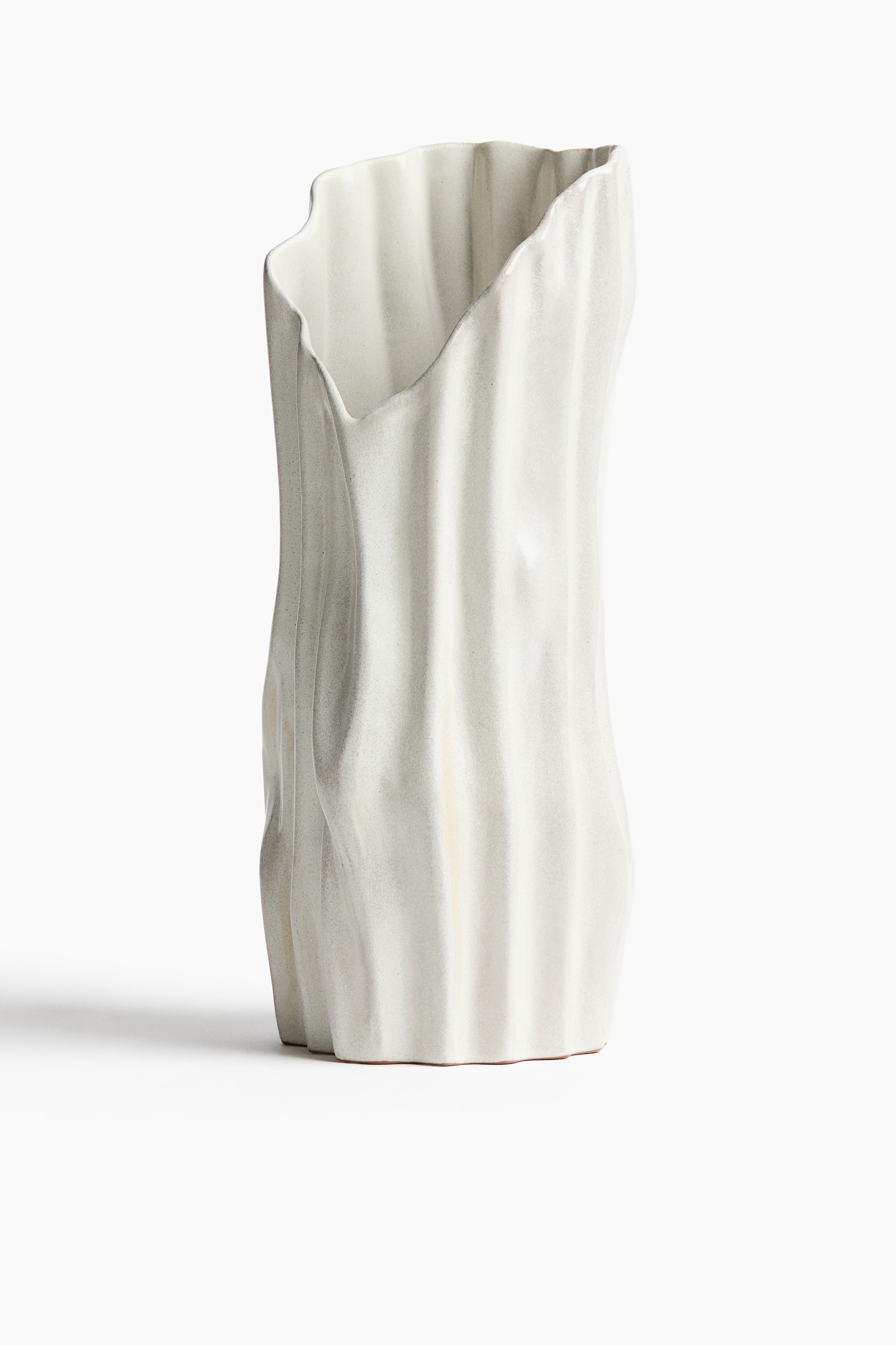 A sculptural, off-white ceramic vase stands upright, featuring a textured, wavy surface with vertical ridges and an asymmetrical rim. The vase holds dried, reddish-brown eucalyptus branches with small seed pods and oval leaves cascading over the side.