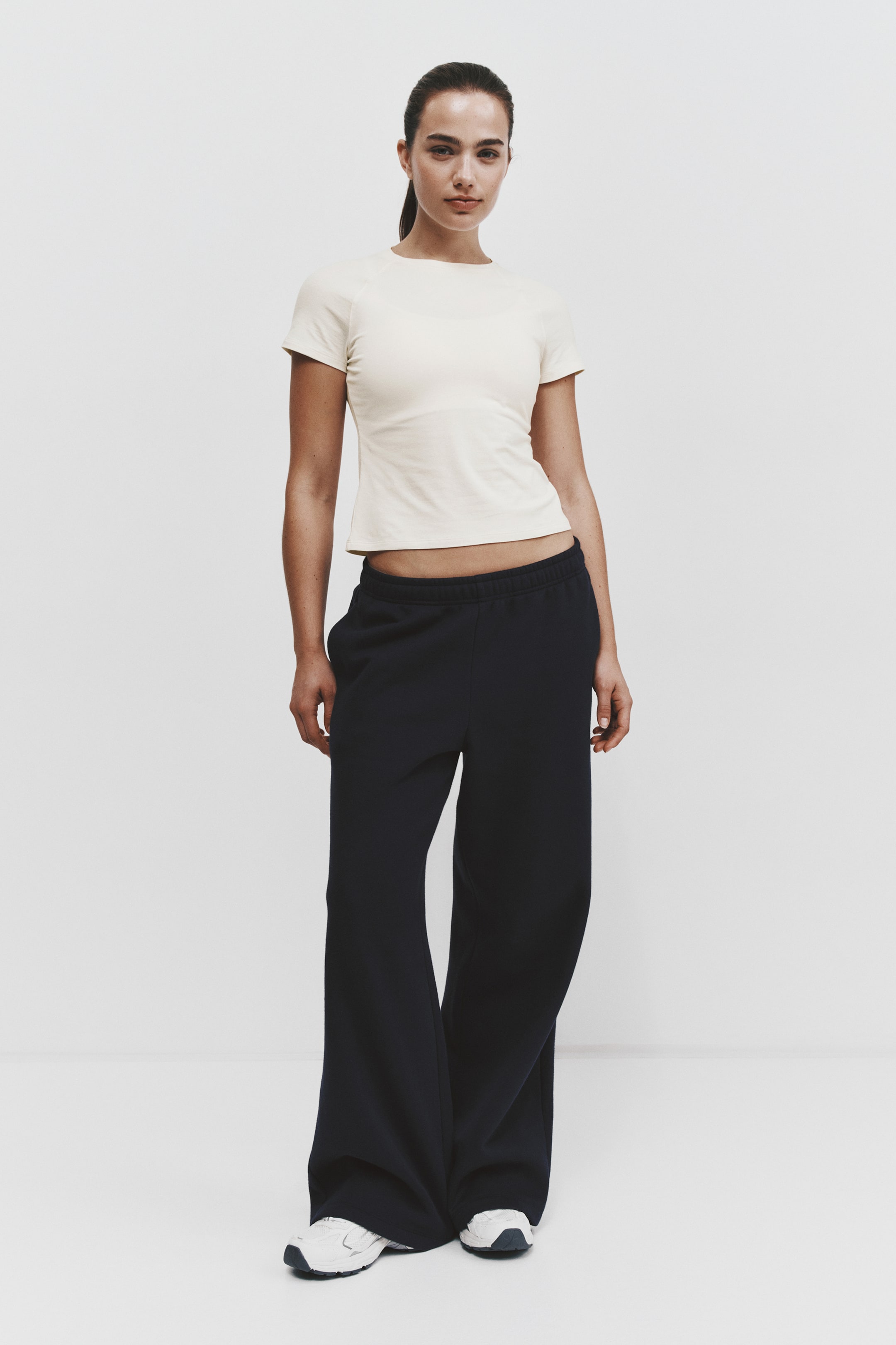 View larger image: A cream-coloured, slim-fit T-shirt with short raglan sleeves is styled with dark navy, wide-leg sweatpants, shown from the front. The relaxed-fit sweatpants feature an elasticated waistband and fall loosely over white sneakers.