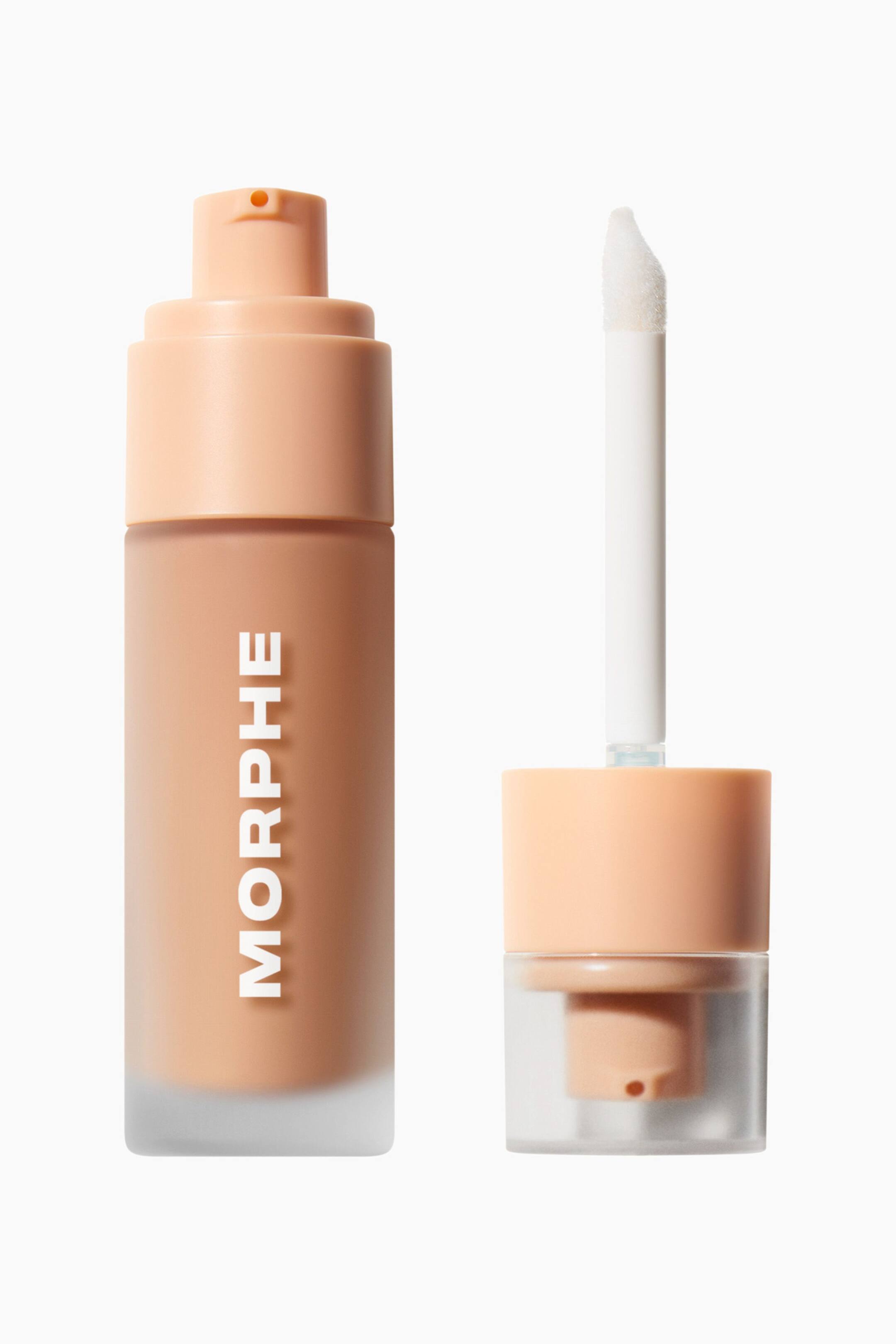 Vis større bilde: En frostet glassflaske som inneholder den ferskenfargede Morphe Complexion Boost Peptide Glow Serum står oppreist, med en vertikal hvit brandlogo og en ferskenfarget pumpe. Ved siden av flasken ligger den løse, klare hetten opp ned, og viser en integrert hvit stav med en skrå doe-foot-applikator som strekker seg oppover.