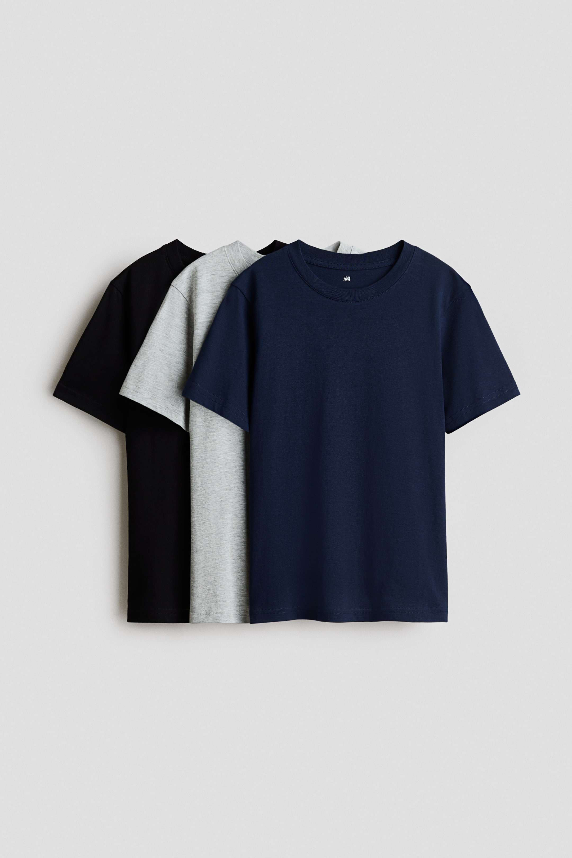 View larger image: Round-neck T-shirts are displayed in a set of three, layered with their fronts facing forward. The frontmost T-shirt is navy blue, featuring a ribbed crew neck and short sleeves, while a light gray melange T-shirt and a black T-shirt are partially visible behind it.