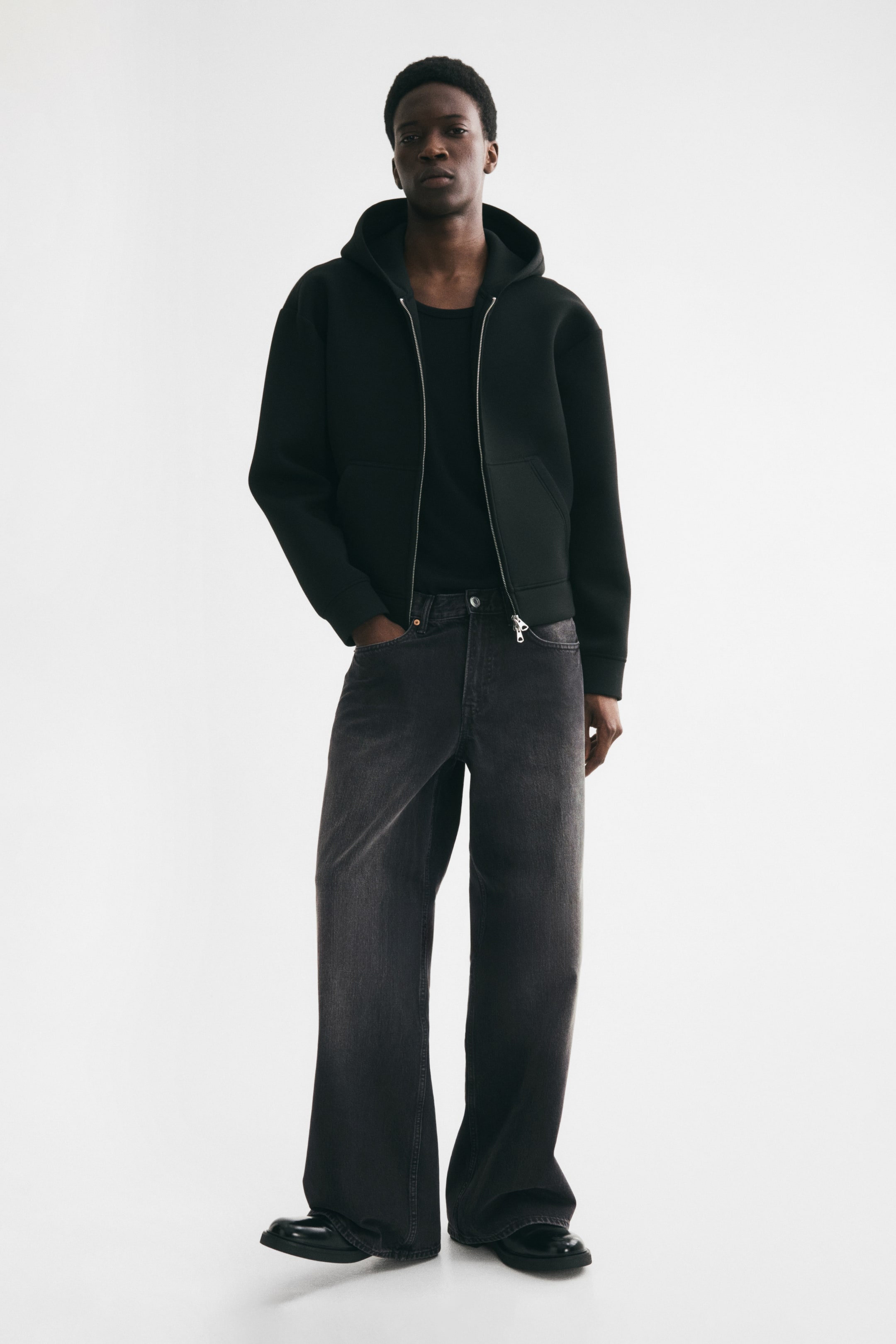 View larger image: 5-pocket jeans in dark grey rigid cotton denim are being worn by the model. The jeans feature a loose fit from the seat to the hem with a dropped crotch and wide legs, a regular waist, and a zip fly with a button closure.