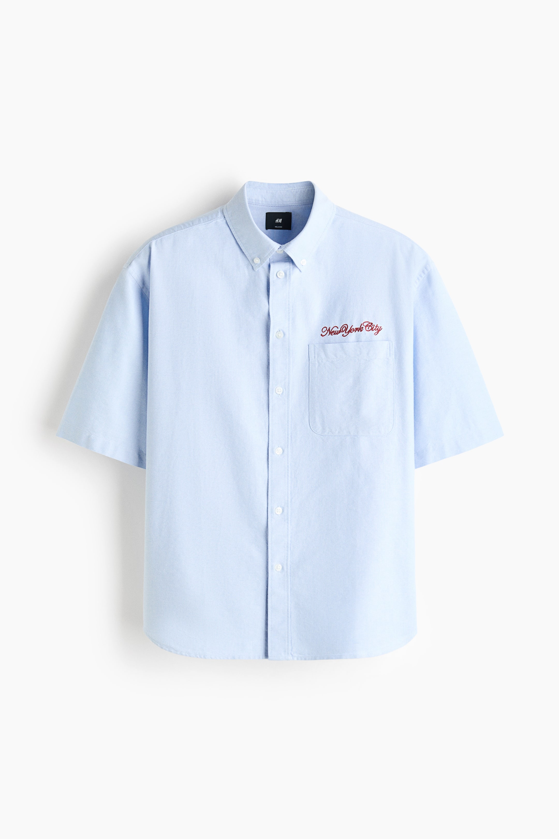 View larger image: The light blue shirt is shown in a front view, highlighting a button-down collar and a classic button-up front. It features short sleeves, an open chest pocket on the left chest with red embroidered "New York City" text, and a gently rounded hem, offering a relaxed fit.