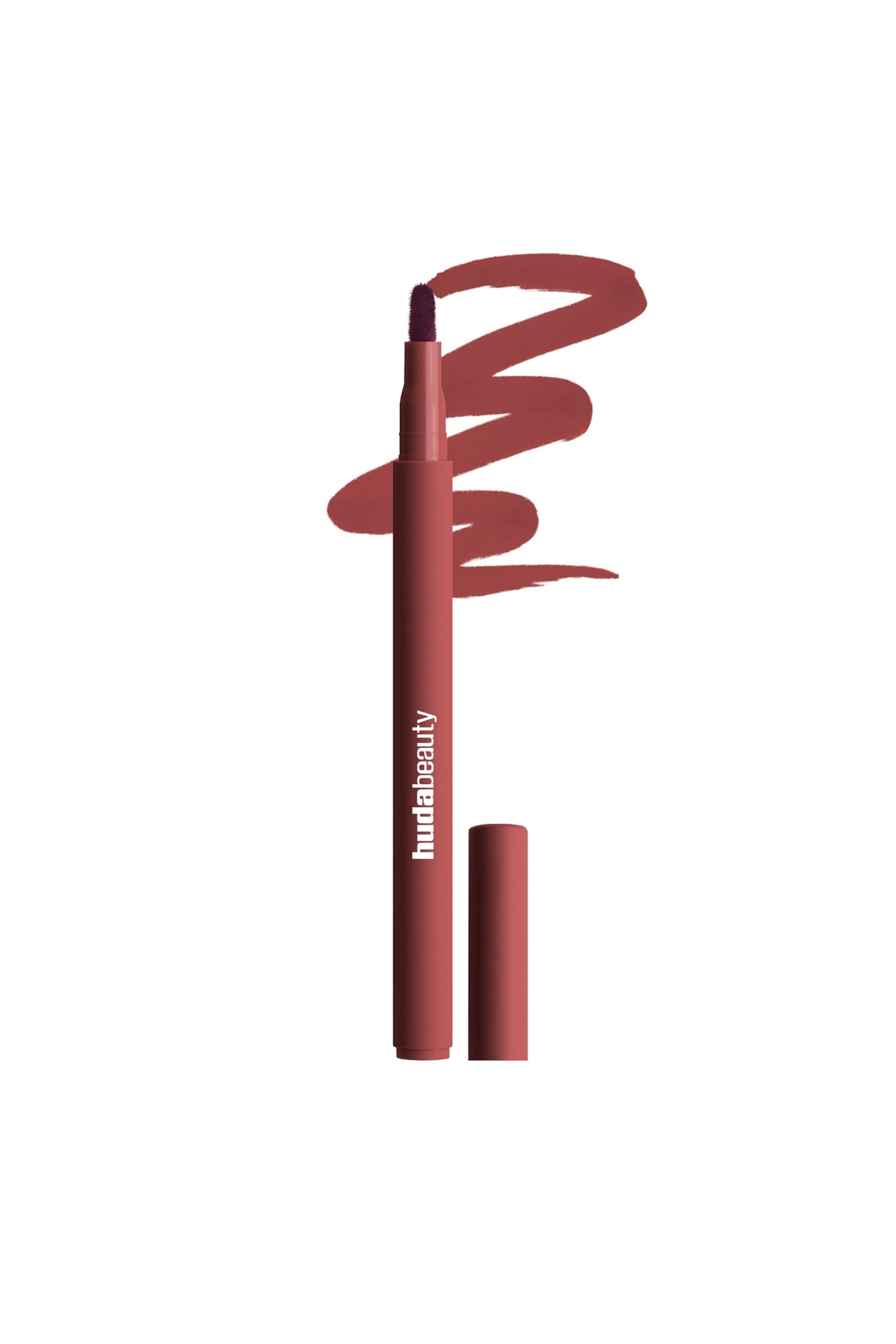 Näytä suurempi kuva: Huda Beauty -huulikynä seisoo pystyasennossa, ja sen mattapintaisessa punaruskeassa rungossa on valkoisella teksti 'hudabeauty'; tummempi luumunvärinen sivellinkärki on näkyvissä. Sitä vastaava punaruskea korkki lepää sen tyvellä, ja punaruskean tuotteen pyörteilevät linjat näkyvät kynän takana.