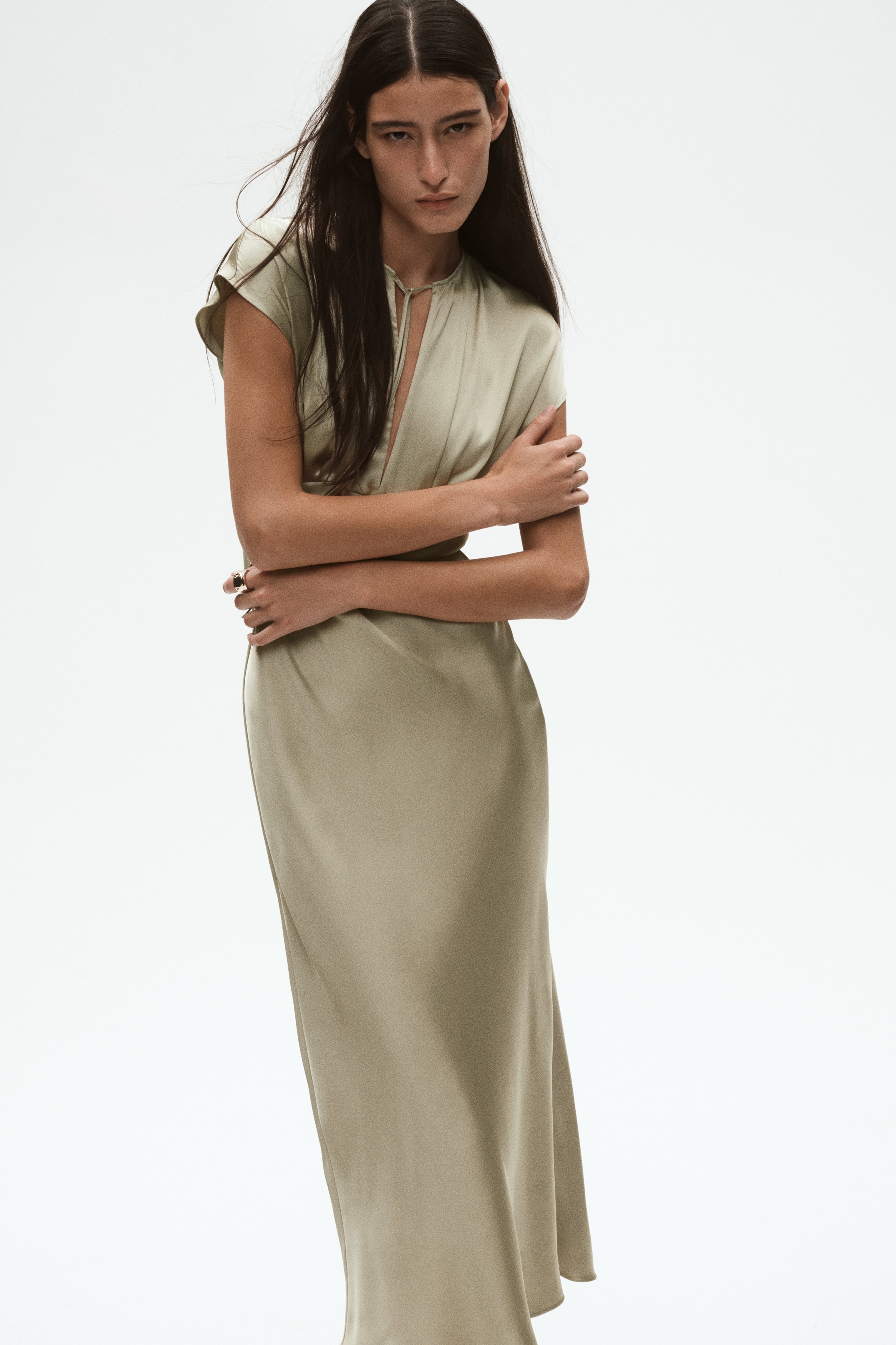 Dieses satinierte Kleid in hellem OlivgrÃ¼n hÃ¤ngt frontal und zeigt einen Rundhalsausschnitt mit zentralem Cut-out und zarten BindebÃ¤ndern. Das Design verfÃ¼gt Ã¼ber Raffungen unter der Brust, drapierte KappenÃ¤rmel und einen fliessend fallenden, gerade geschnittenen Rock.