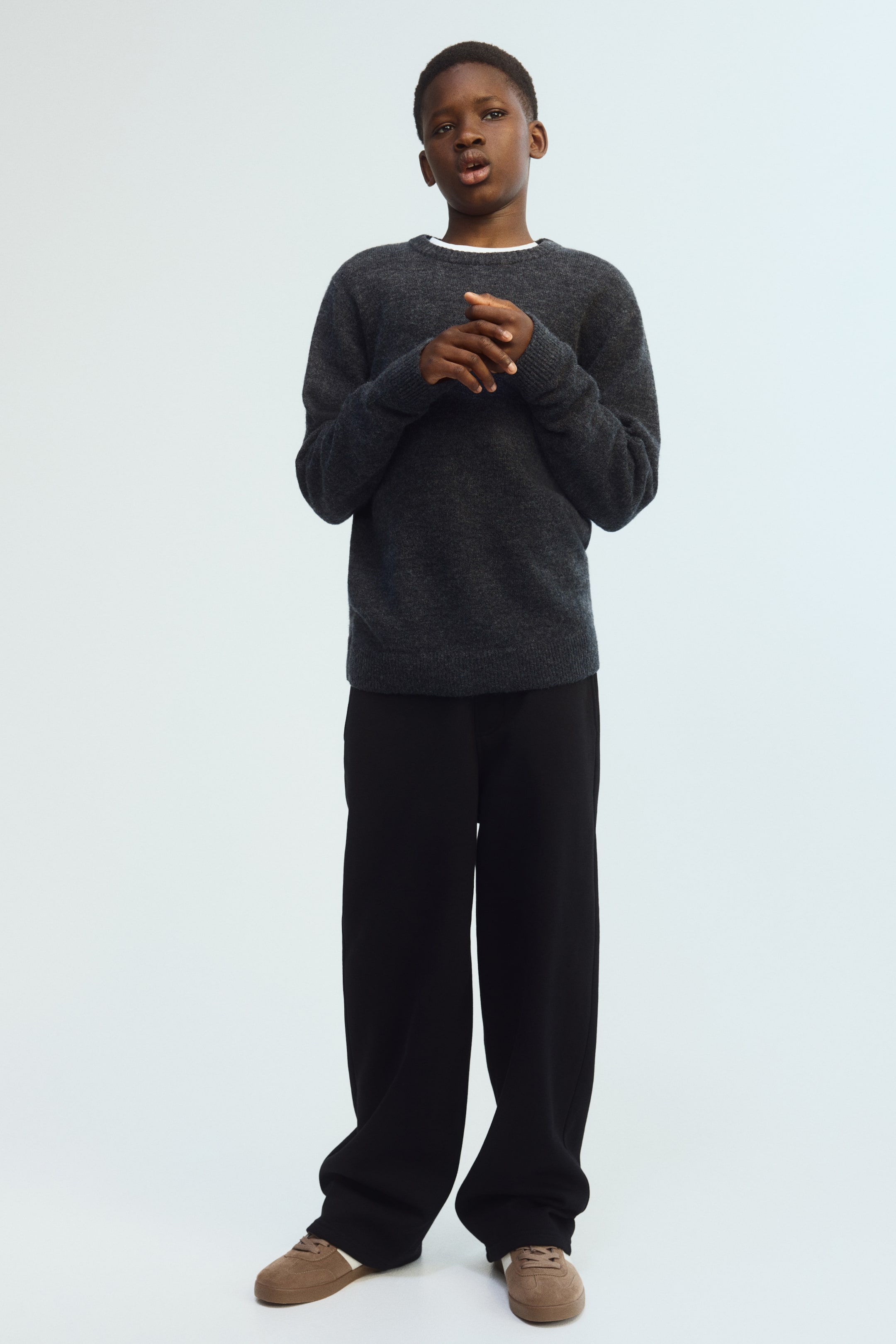 View larger image: A charcoal gray crew neck sweater is worn, showcasing ribbed cuffs and hem, with a white tee visible underneath. Black wide-leg pants complement the look, offering a relaxed fit and gently pooling at the ankles.