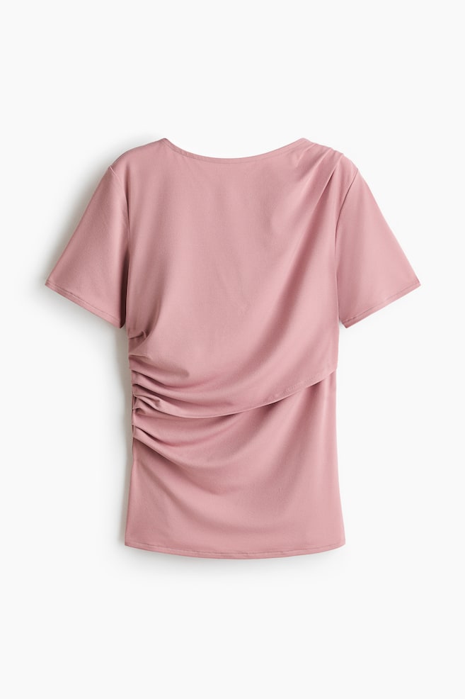 The MAMA Draped nursing top is shown from the back in a dusty-rose colour, featuring a round neckline and short sleeves. Pronounced ruching gathers at the left side seam, forming a draped panel that extends across the lower back. - 1