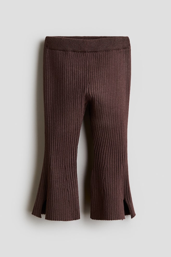 A pair of dark brown rib-knit pants is shown from the front, highlighting a vertical ribbed texture and a thick elasticated waistband. The legs flare towards the hem, which features small slits on the outer sides. - 1