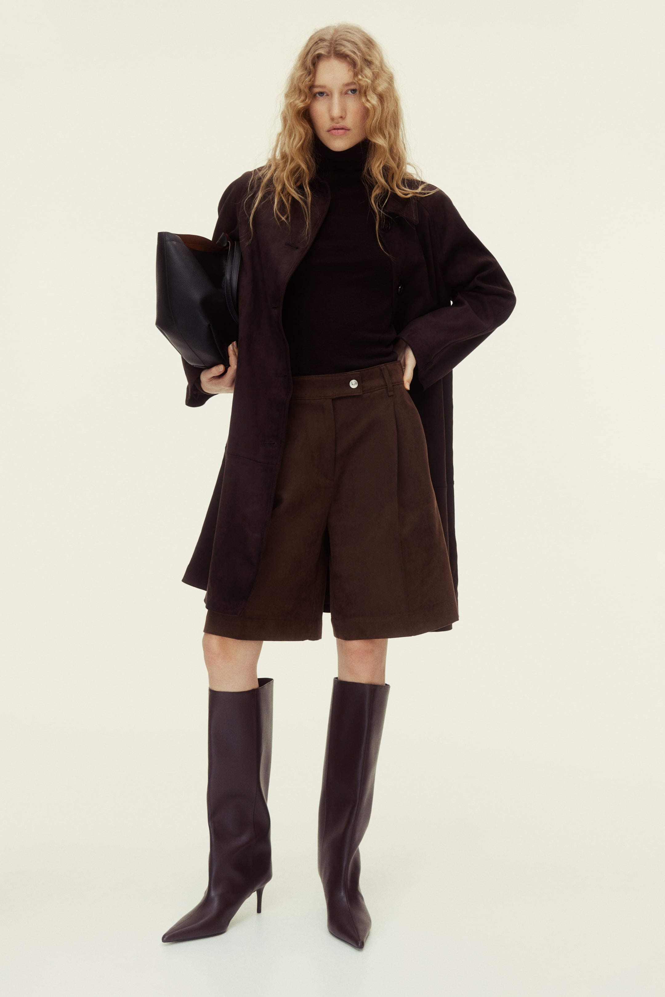 Größeres Bild anzeigen: Braune Cord-Shorts werden von vorne gezeigt, verfügen über einen High-Waist-Bund mit einem sichtbaren Knopfverschluss und weisen markante vordere Falten auf. Sie sind im Wide-Leg-Schnitt gearbeitet und reichen knapp über das Knie.