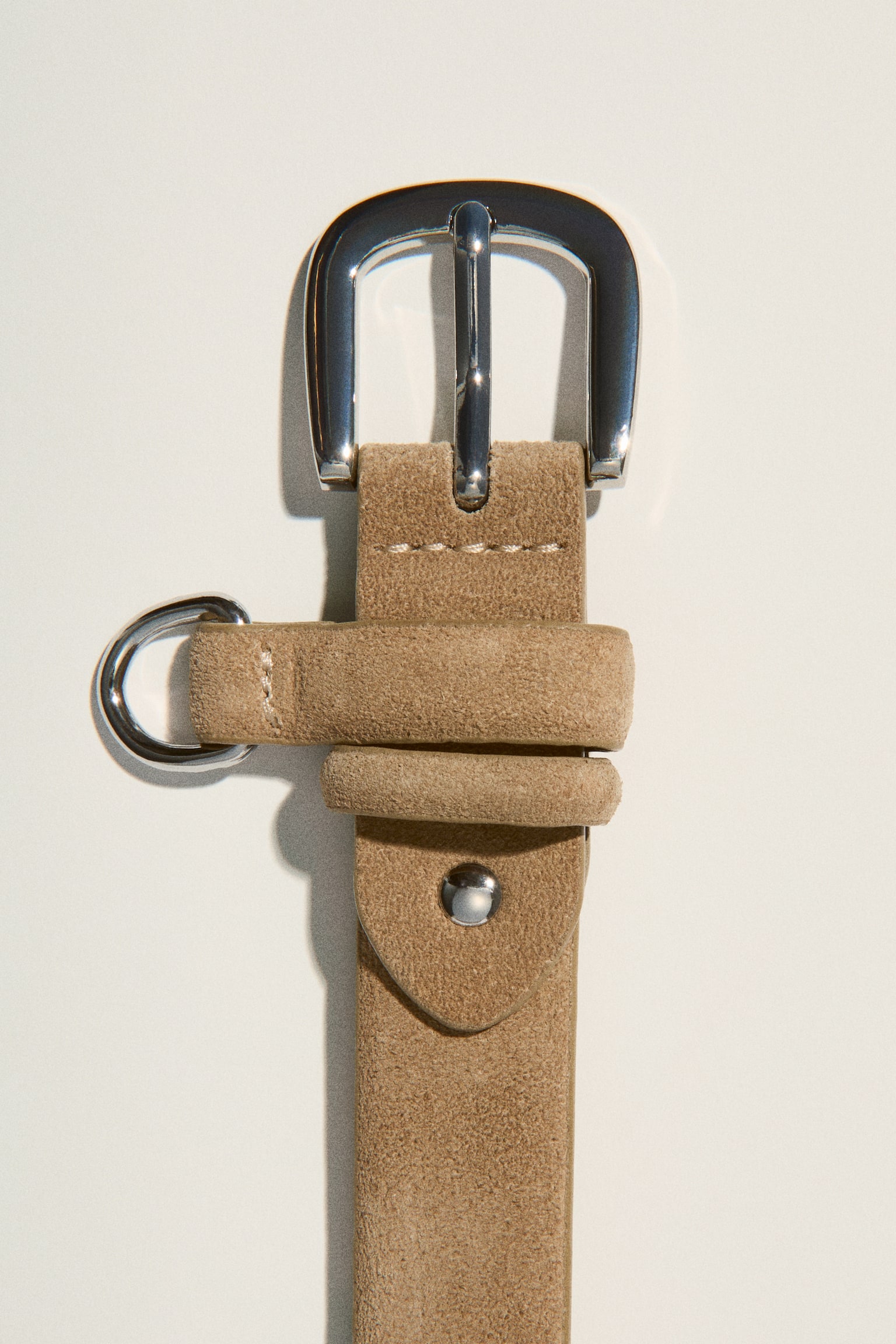 A tan suede belt is lying flat and vertically, featuring a silver-toned pin buckle, two keeper loops, and an attached silver-toned O-ring. - 1