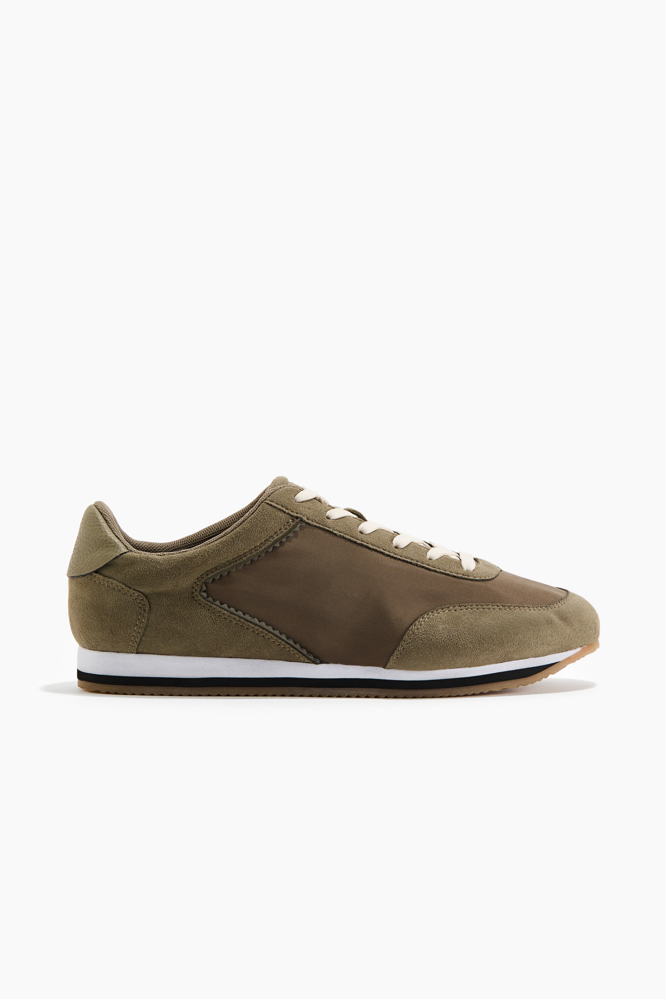 View larger image: The olive green sneaker showcases a mixed-material upper, with suede overlays gracing the toe, heel, and eyelets, complemented by a textile panel with a scalloped edge. Cream laces weave through the eyelets, while a white midsole featuring a black stripe sits atop a brown outsole.