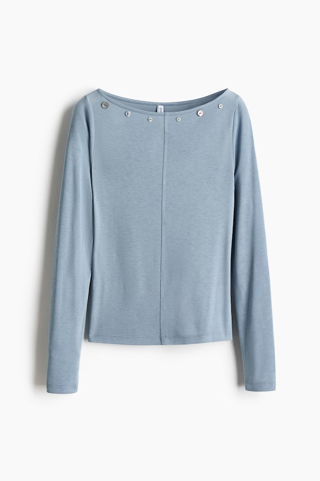 A light blue, long-sleeved top in a soft stretch jersey is shown facing front, featuring a wide boat neckline adorned with decorative pearly buttons. The design includes a distinct vertical seam running down the center front. - 1