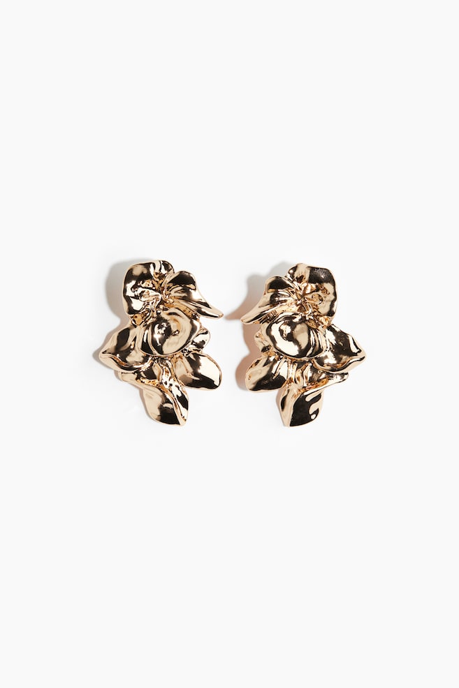 Two gold-toned earrings are lying side-by-side, each featuring an abstract, sculptural design of crumpled and overlapping metallic shapes. Their surfaces are shiny and highly reflective. - 1