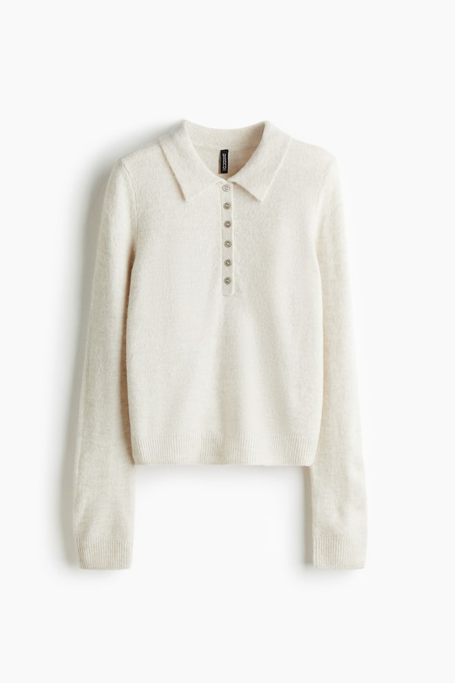 A cream-colored knit polo sweater is presenting a front view, featuring a pointed collar and a six-button placket. It is designed with long sleeves, ribbed cuffs, and a ribbed hem. - 1