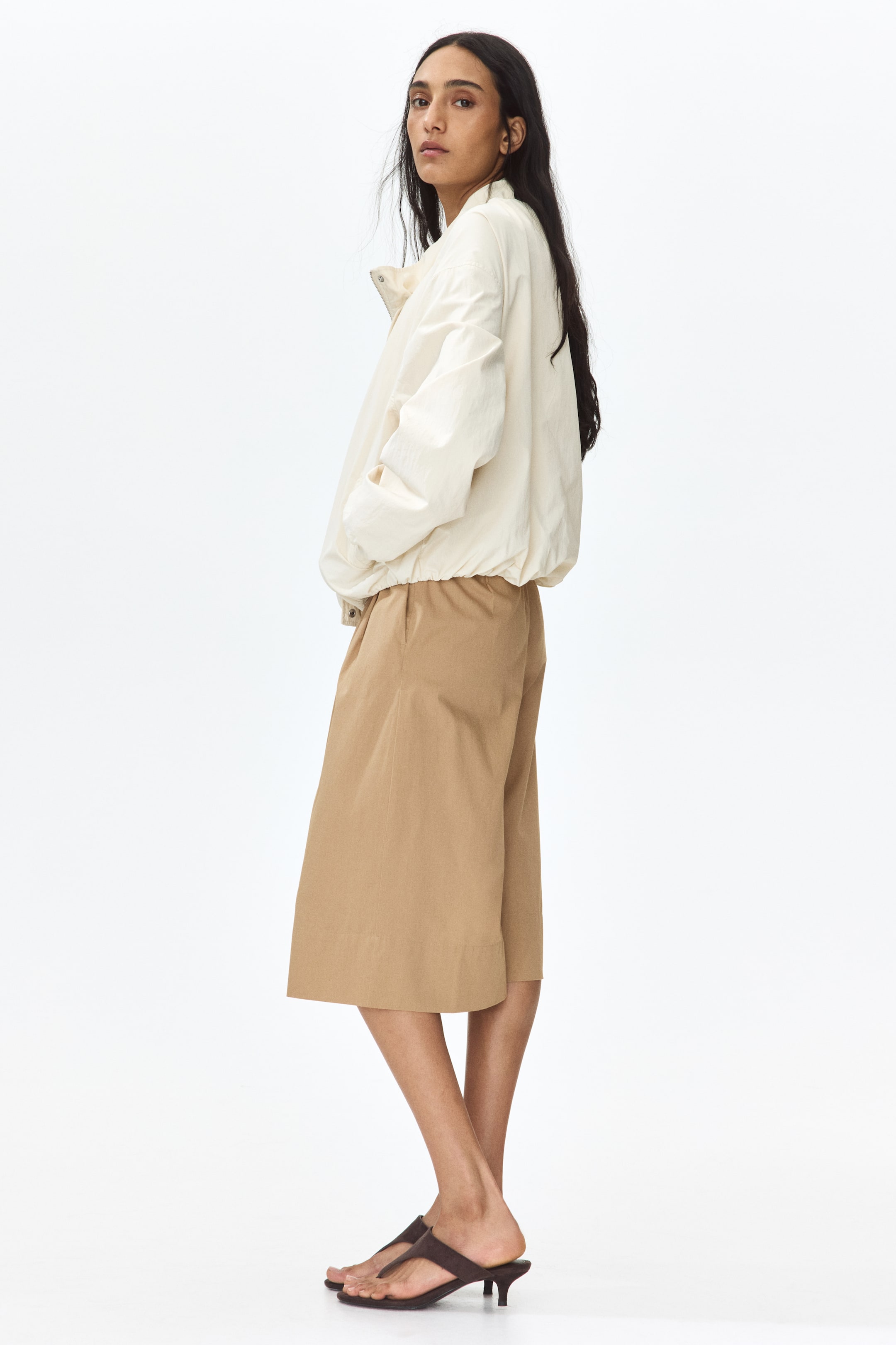View larger image: Knee-length, relaxed-fit shorts are showcasing a high waist, subtle front pleats, and diagonal side pockets. The product is being displayed from a side-front angle.