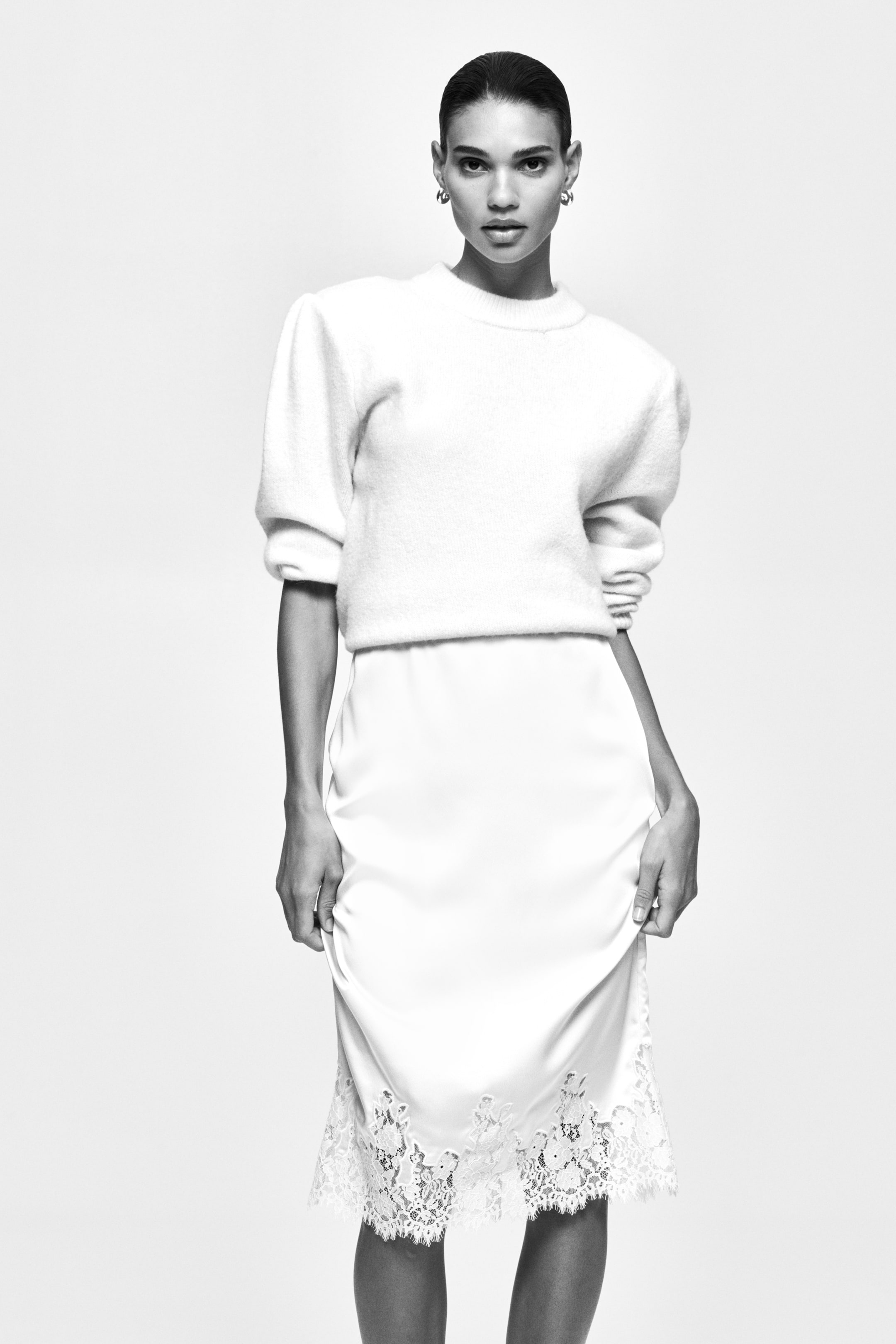 View larger image: A white, fuzzy knit jumper features puffed, elbow-length sleeves and a crew neck, resting at the waist. A smooth, white slip skirt layers underneath, showcasing intricate lace trim along its hem and falling below the knee.