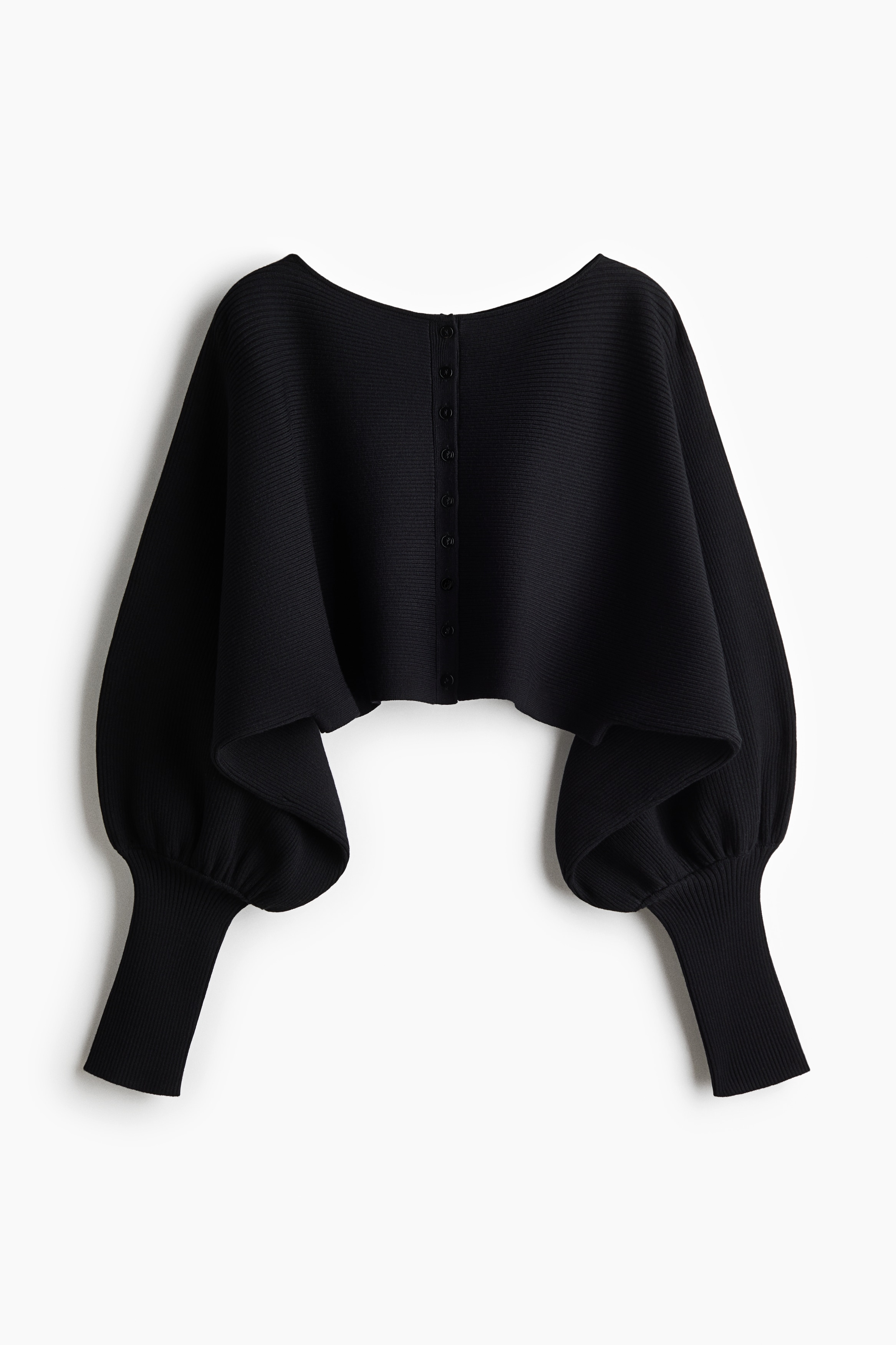 A black cropped cardigan in a fine rib knit is worn by the model, showcasing a loose fit with long cape sleeves and wide, close-fitting cuffs. The cardigan is styled with leopard-print bottoms and a light grey sweatshirt tied around the waist.