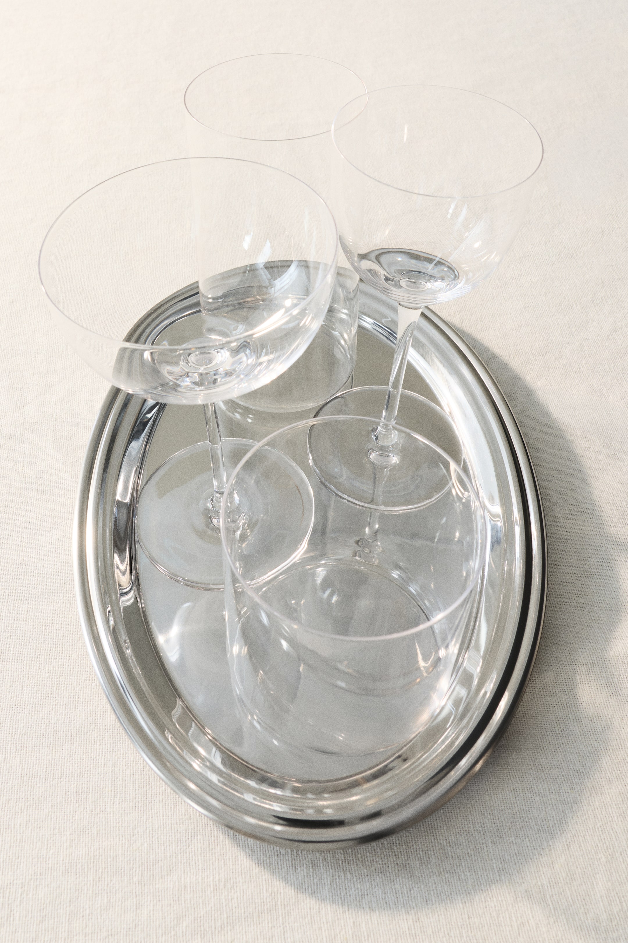 Ver imagen más grande: Una bandeja redonda de color plateado exhibe dos copas coupette de cristal transparente con tallo y dos vasos de cristal transparente, todos dispuestos sobre su superficie y vistos desde un ángulo ligeramente elevado.