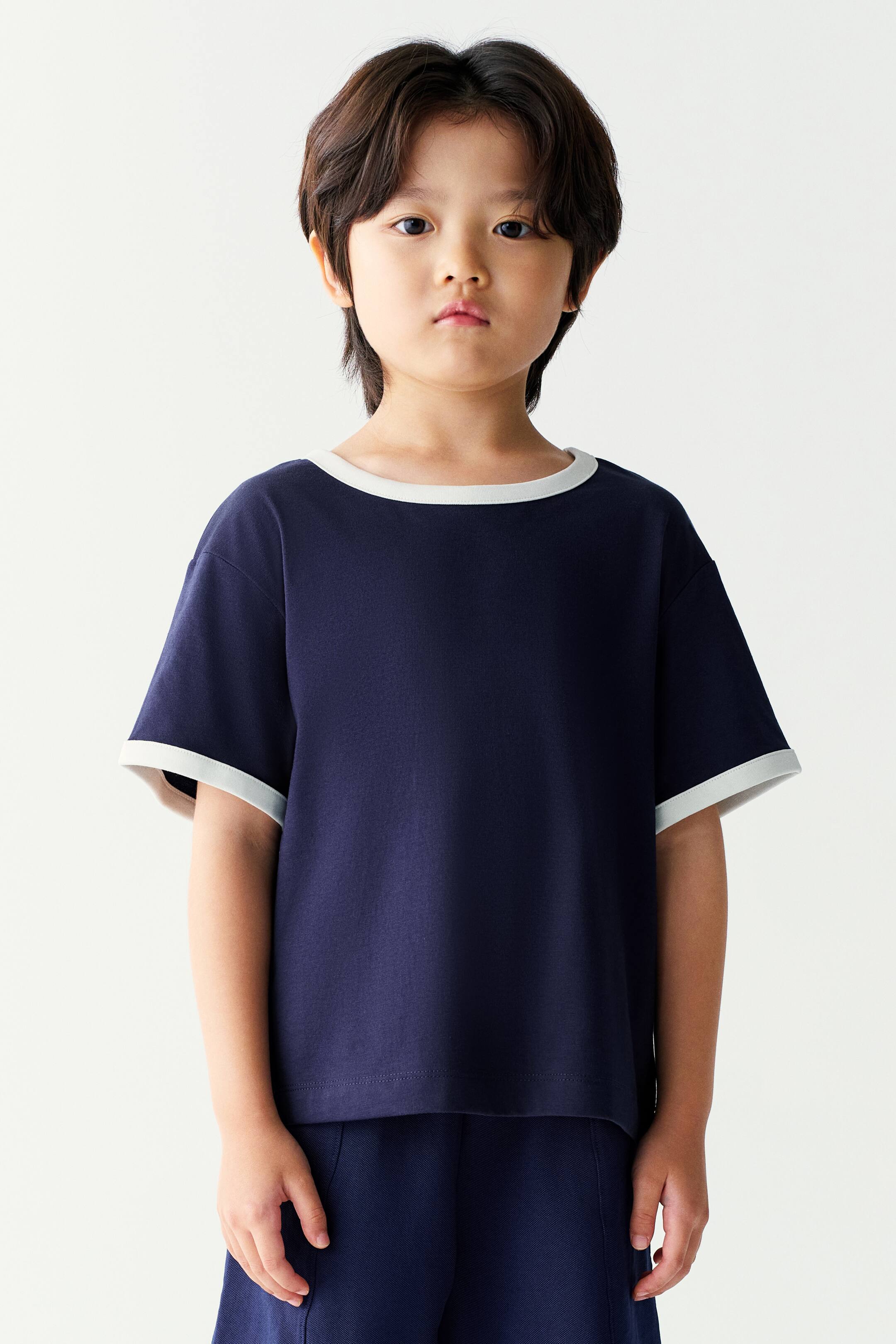View larger image: A navy blue short-sleeved t-shirt featuring a contrasting off-white crew neck and matching sleeve cuffs is worn by the model. The t-shirt is styled with matching navy blue shorts.