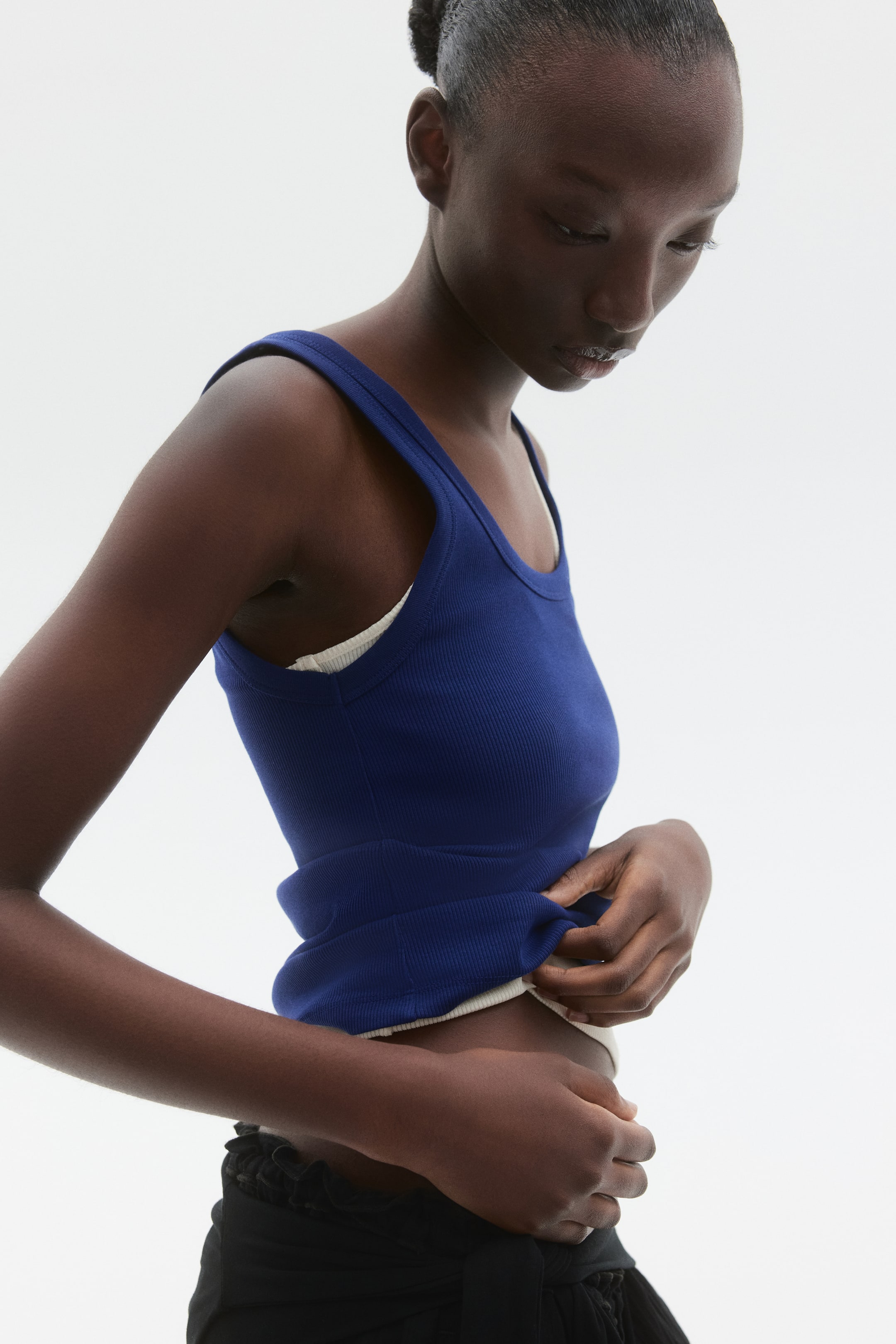 Voir une image plus grande: Un débardeur ajusté en jersey de coton côtelé bleu marine est porté par le mannequin. Un haut côtelé de couleur claire est superposé en dessous, et le mannequin tient et soulève légèrement l'ourlet du haut bleu marine.